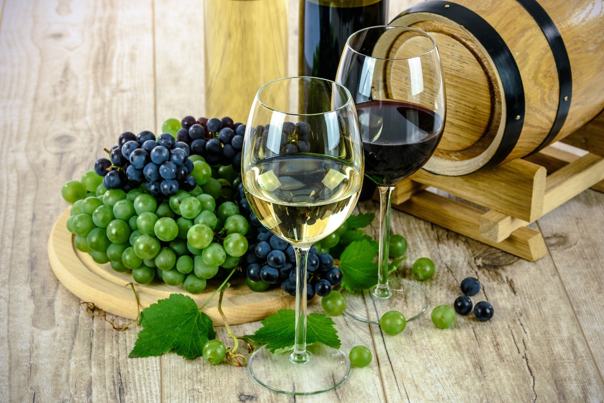 A table decked out with red and white wine, a barrel, and some grapes | Photo: by Pixabay/Photo Mix