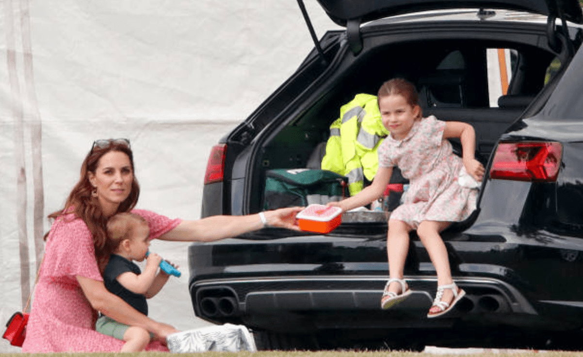 Kate Middleton holds Prince Louis and passes a lunch box to Princess Charlotte as they sit by their car at the King Power Royal Charity Polo Match, on July 10, 2019, England | Source: Getty Images