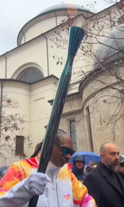Snoop Dogg dances as he holds the lit torch high during the Milano Cortina Olympic torch relay in Gallarate, Italy, posted on February 4, 2026. | Source: X/@milanocortina26