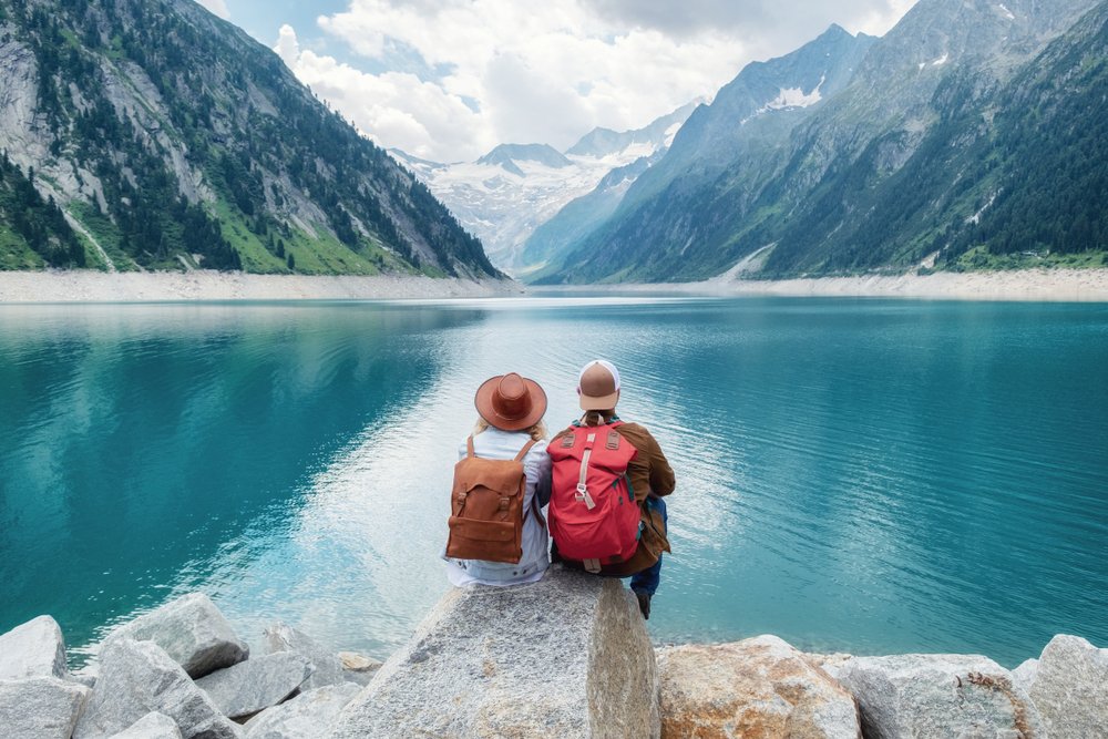 Pareja observando las montañas sentados sobre las rocas frente a un lago. | Foto: Shutterstock