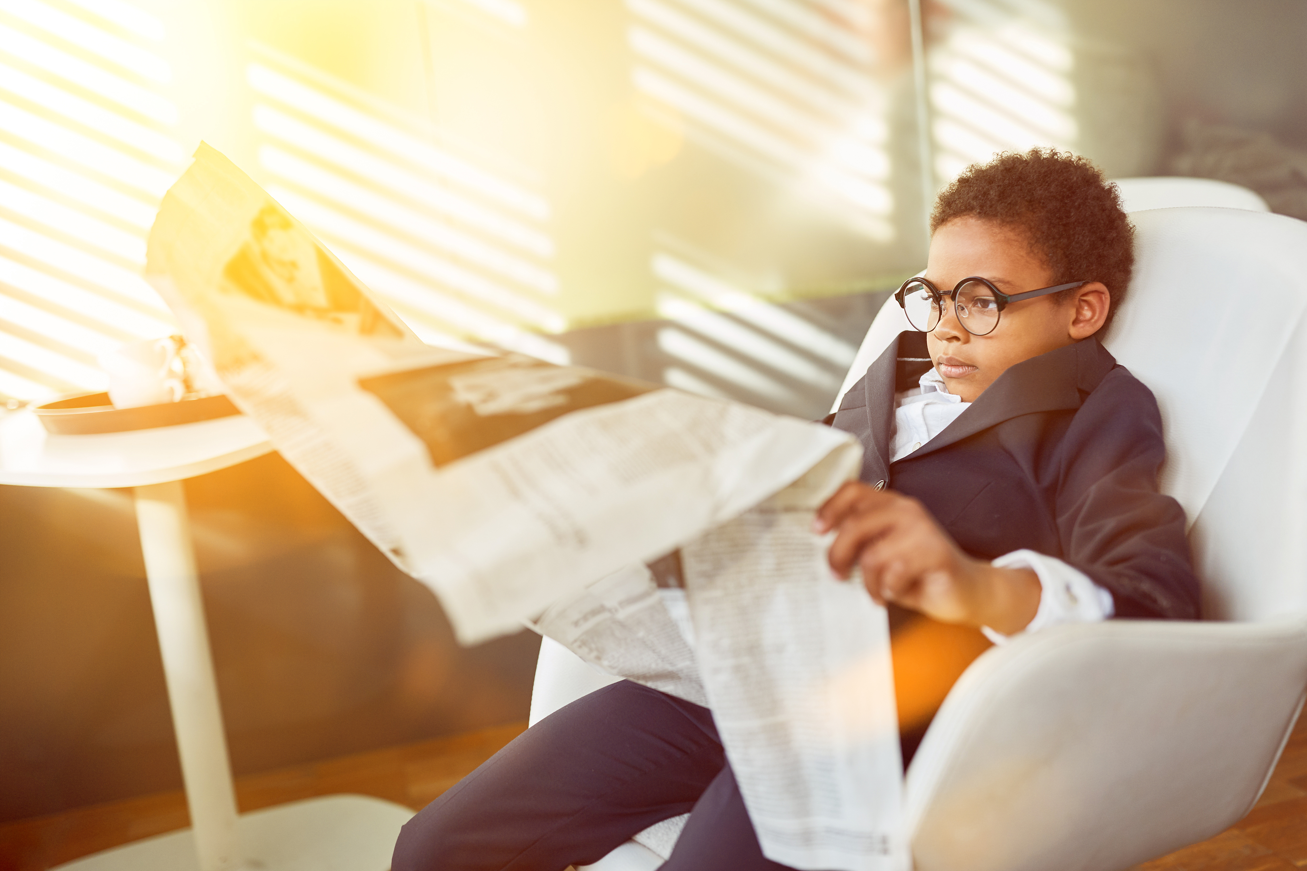 A young boy wearing a suit and spectacles reading the newspaper | Source: Shutterstock
