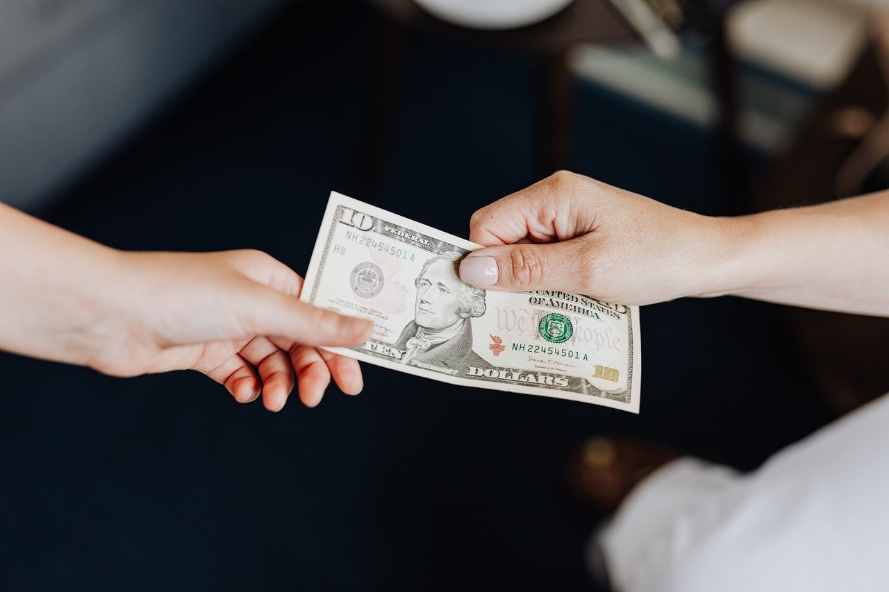 Hands exchanging a $10 bill | Photo: Pexels