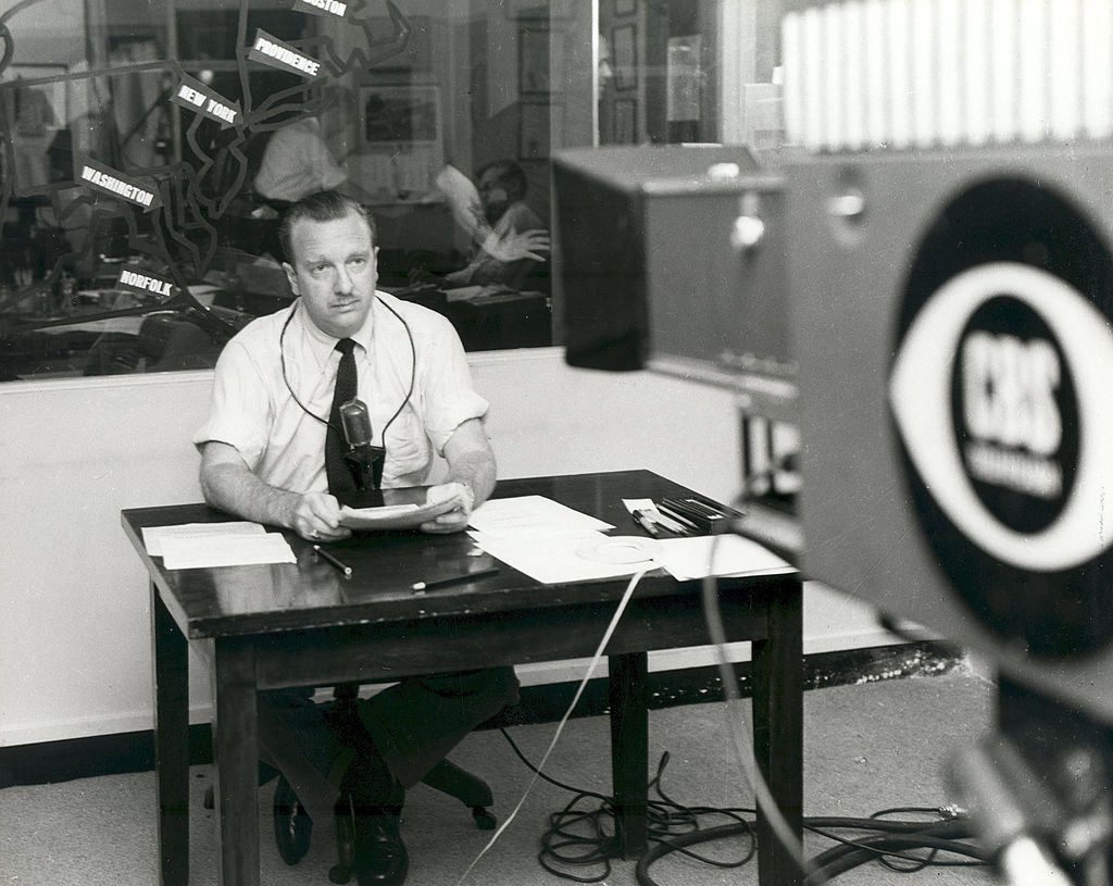 American broadcast journalist Walter Cronkite wears a short sleeved shirt as he sits behind a desk with a microphone around his neck and prepares to read the news, Washington DC, September 11, 1954. | Source: Getty Images