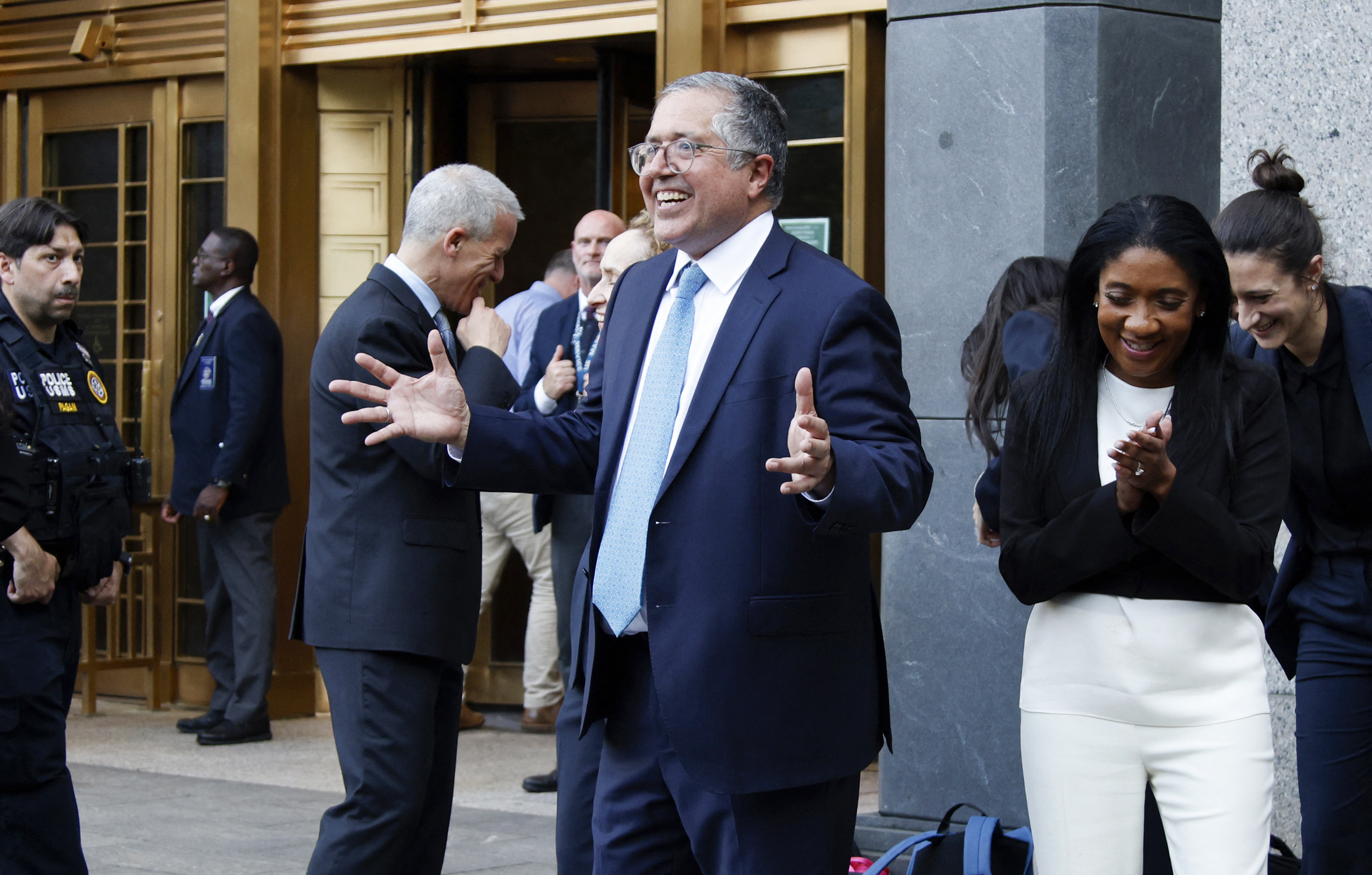 Marc Agnifilo gestures animatedly while exiting the courthouse, flanked by colleagues sharing a moment of visible relief. Smiles and laughter reflect a lightened mood.