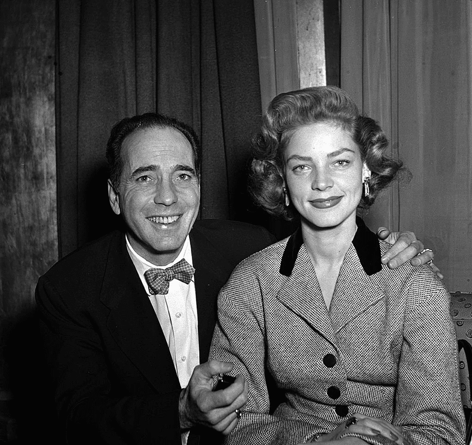 Humphrey Bogart lächelt mit seiner Ehefrau Lauren Bacall bei einer Pressekonferenz bei Claridges in London, 1951. | Quelle: Getty Images