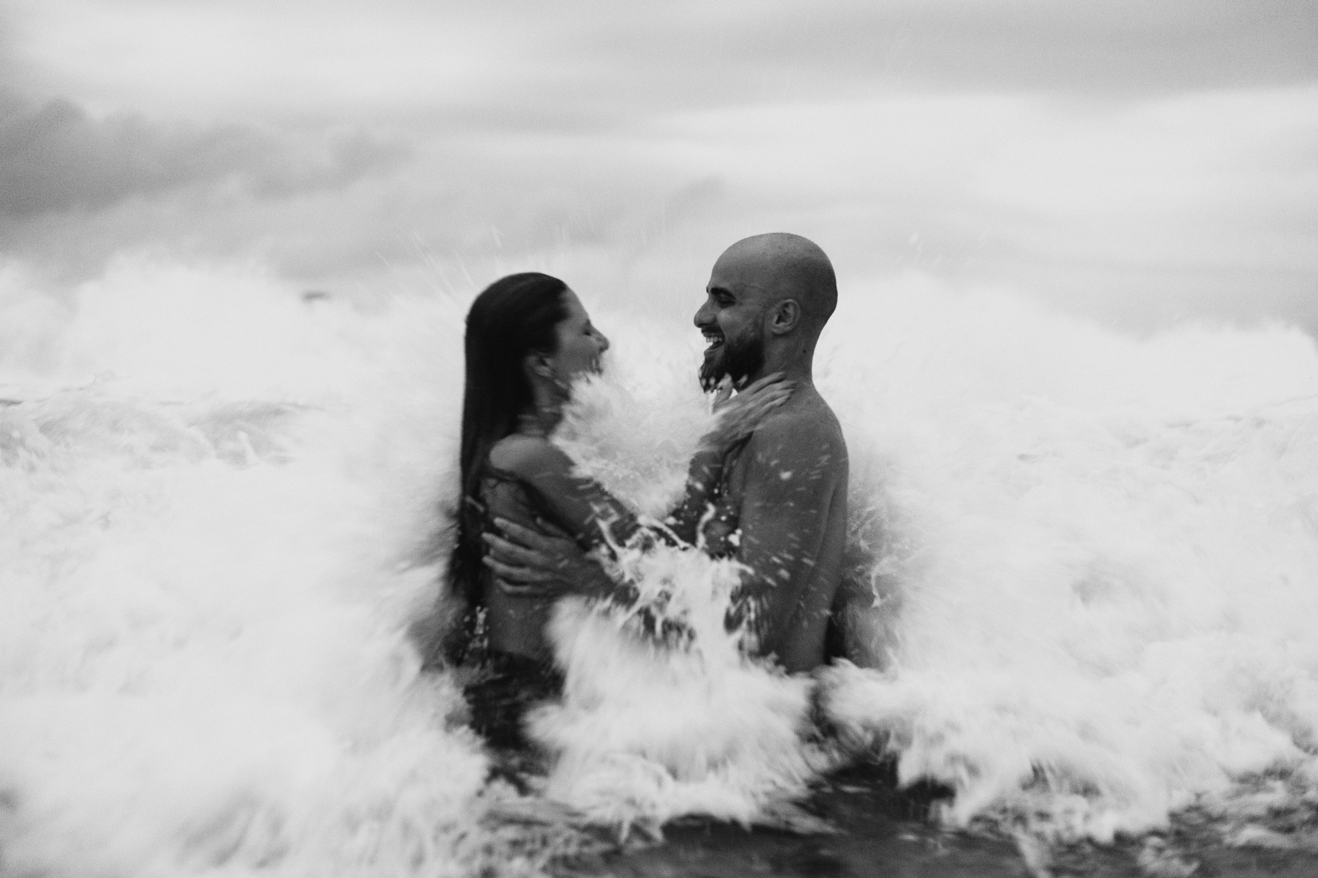 A couple getting hit by a wave. | Source: Pexels