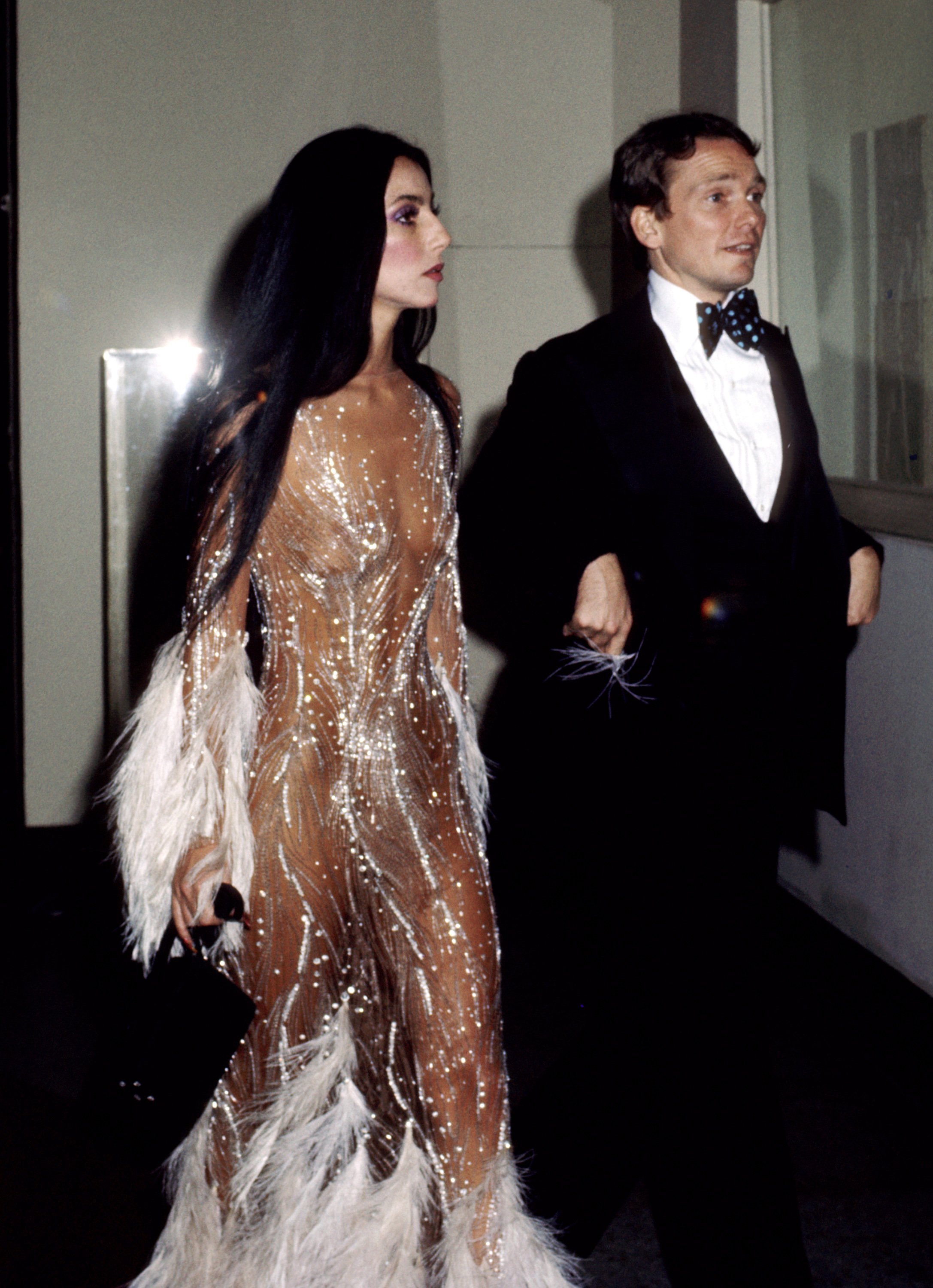 Cher vestida con el vestido ilusión nude de Bob Mackie, escoltada por Bob Mackie en la Gala del Met en 1974 | Foto: Getty Images