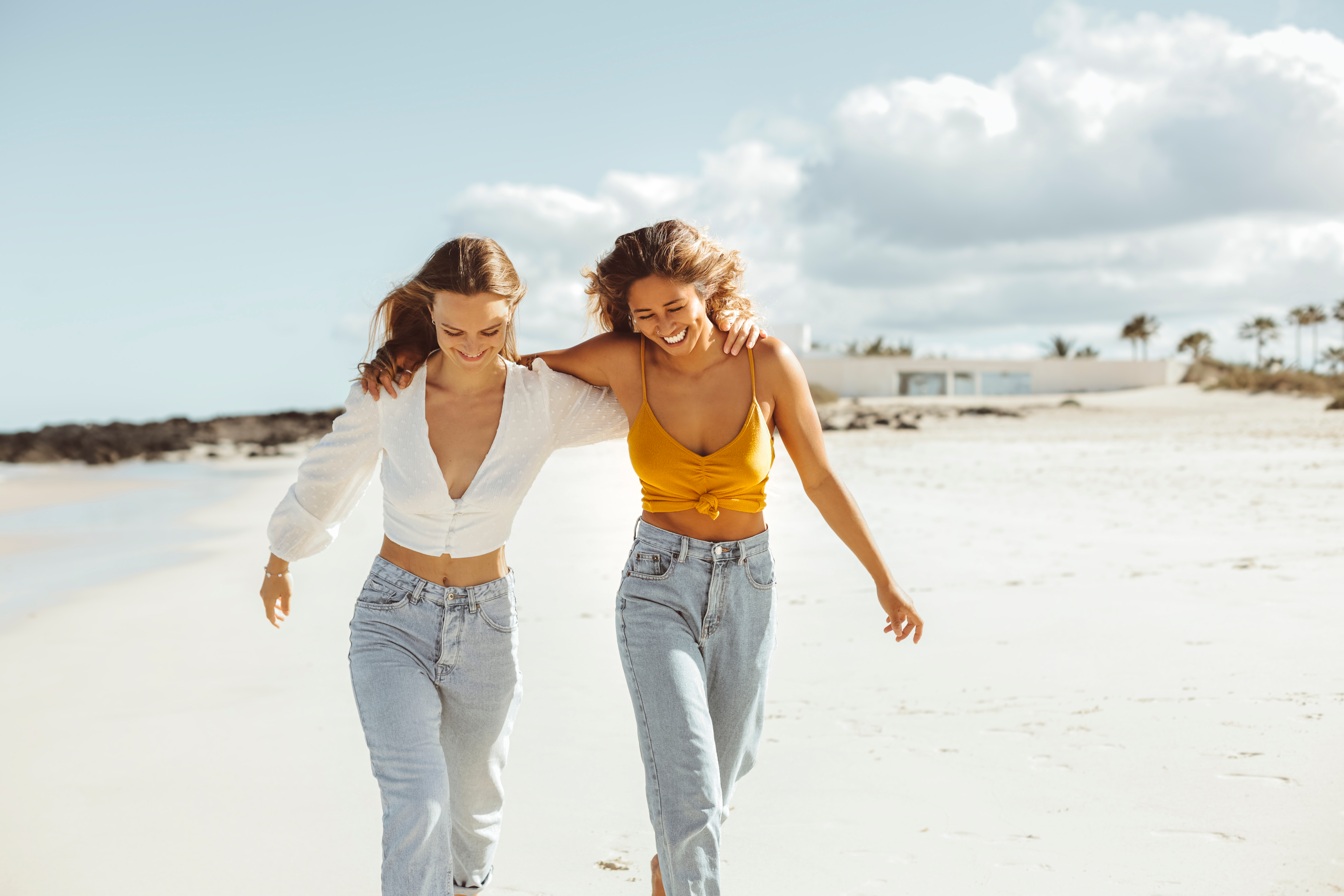 Two best friends walking along a beach and laughing | Source: Shutterstock