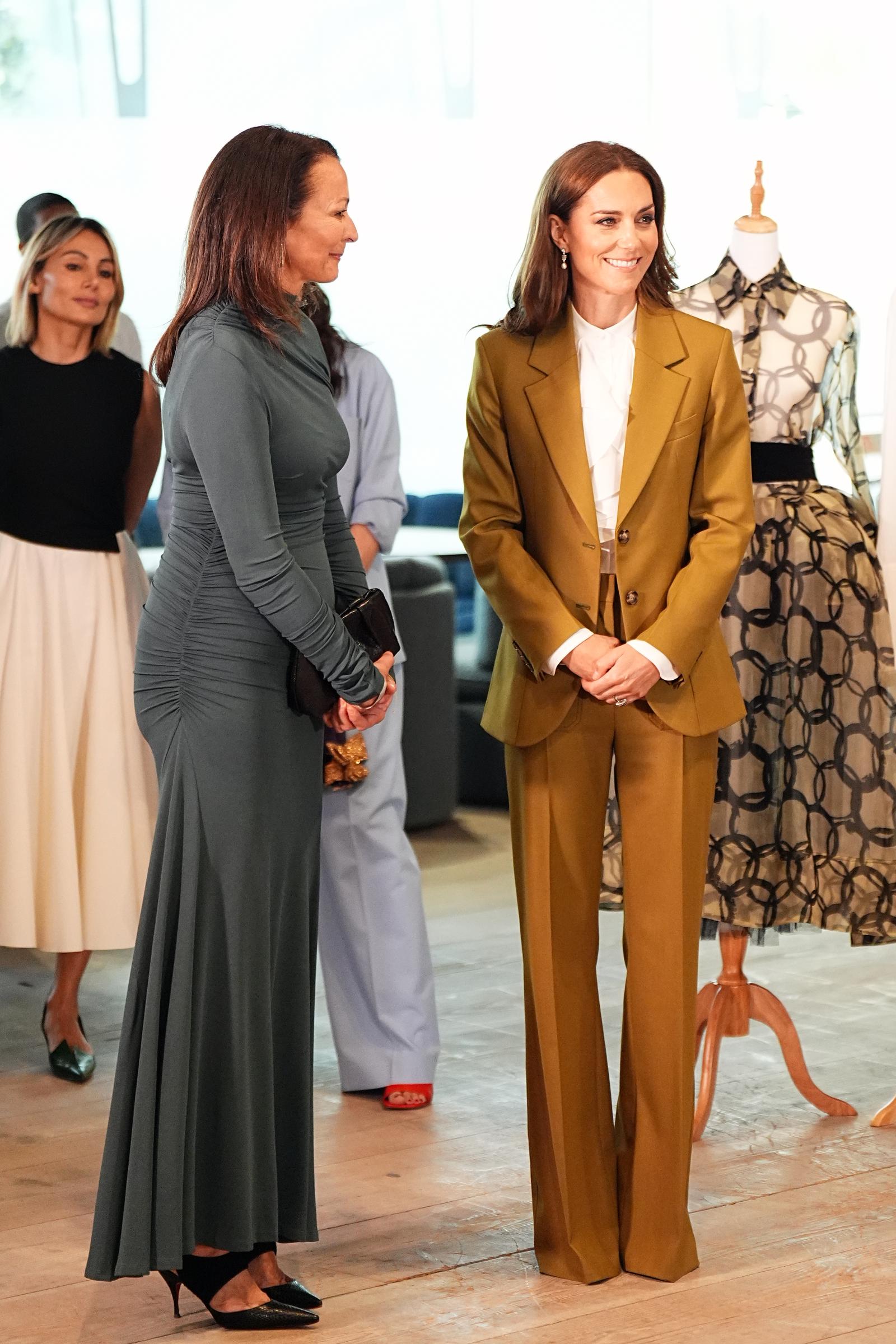 During a tour of the design spaces, Catherine stands engaged in conversation with Caroline Rush. Behind her, a striking dress serves as a backdrop, quietly showcasing the beauty and talent the event was designed to celebrate.