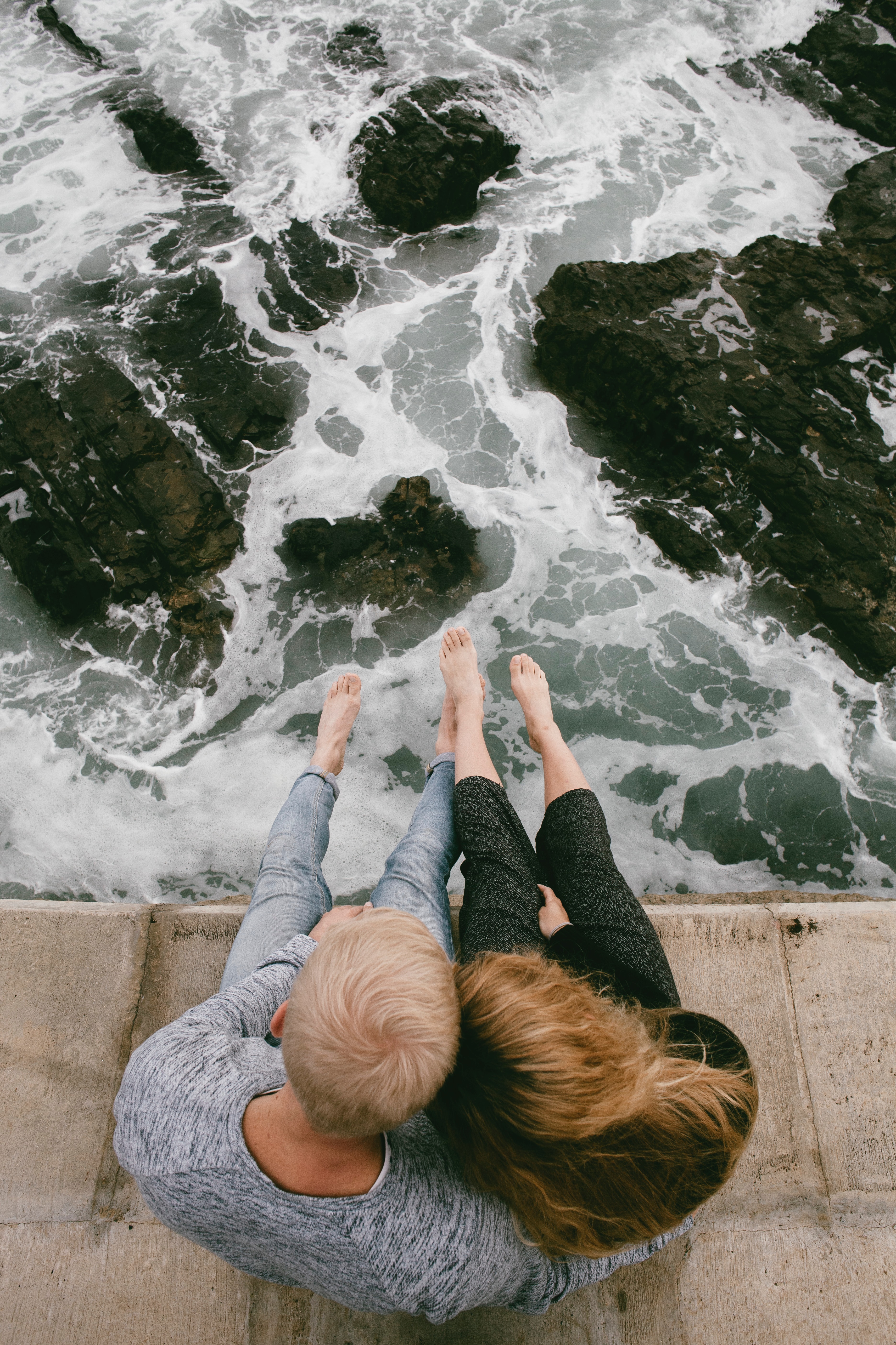 A photo of a couple sitting on a cliff near body of water | Source: Unsplash