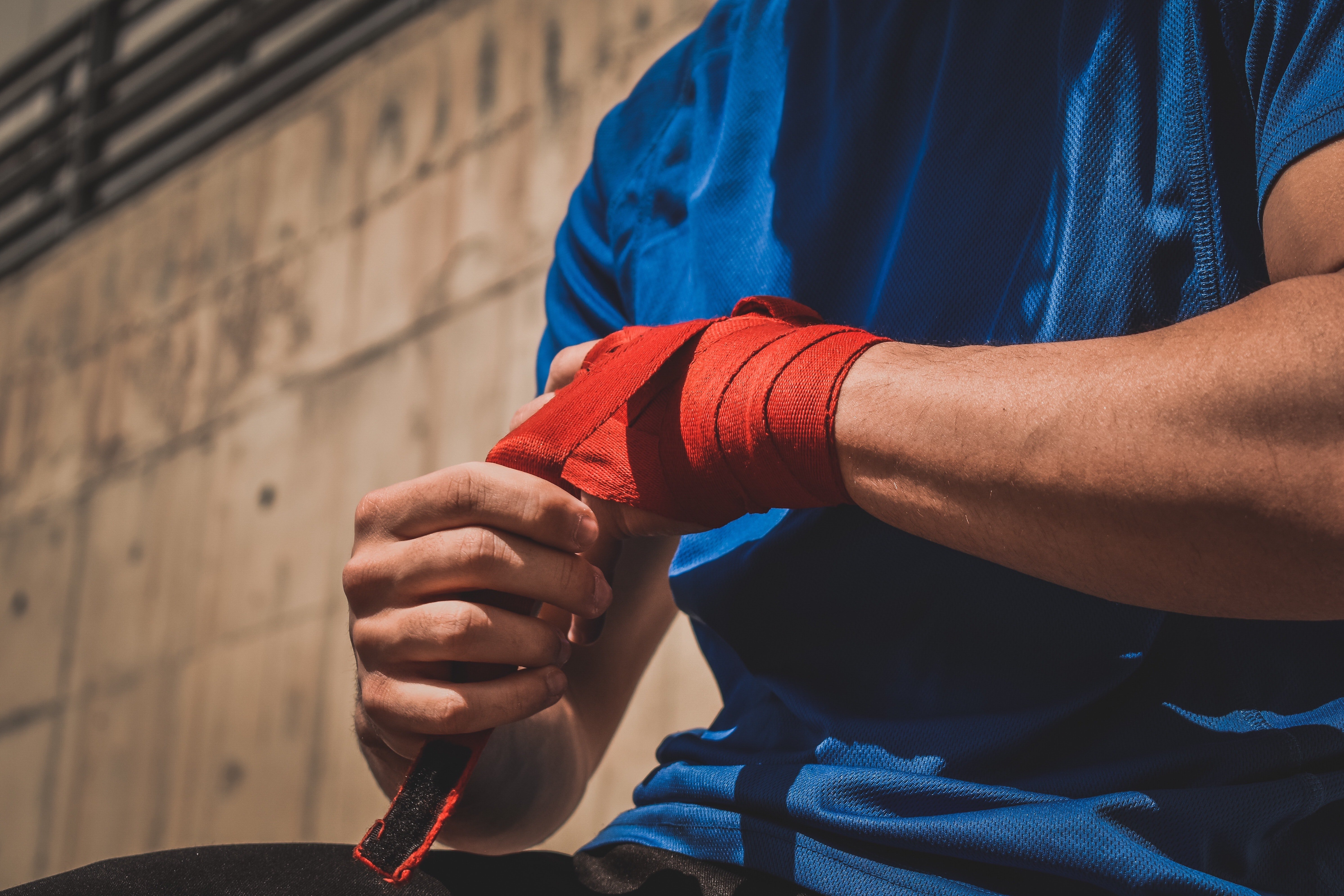 Man wearing a blue T-shirt and fixing his boxing hand wrap  | Source: Unsplash / Payam Tahery