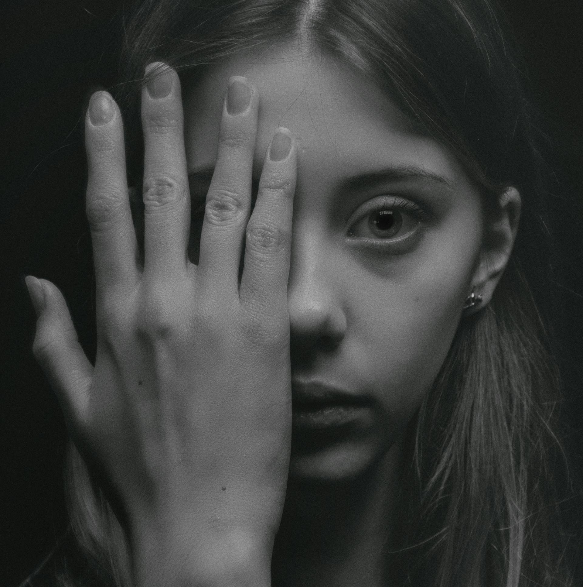 A grayscale photo of a young woman hiding half of her face with one hand | Source: Pexels