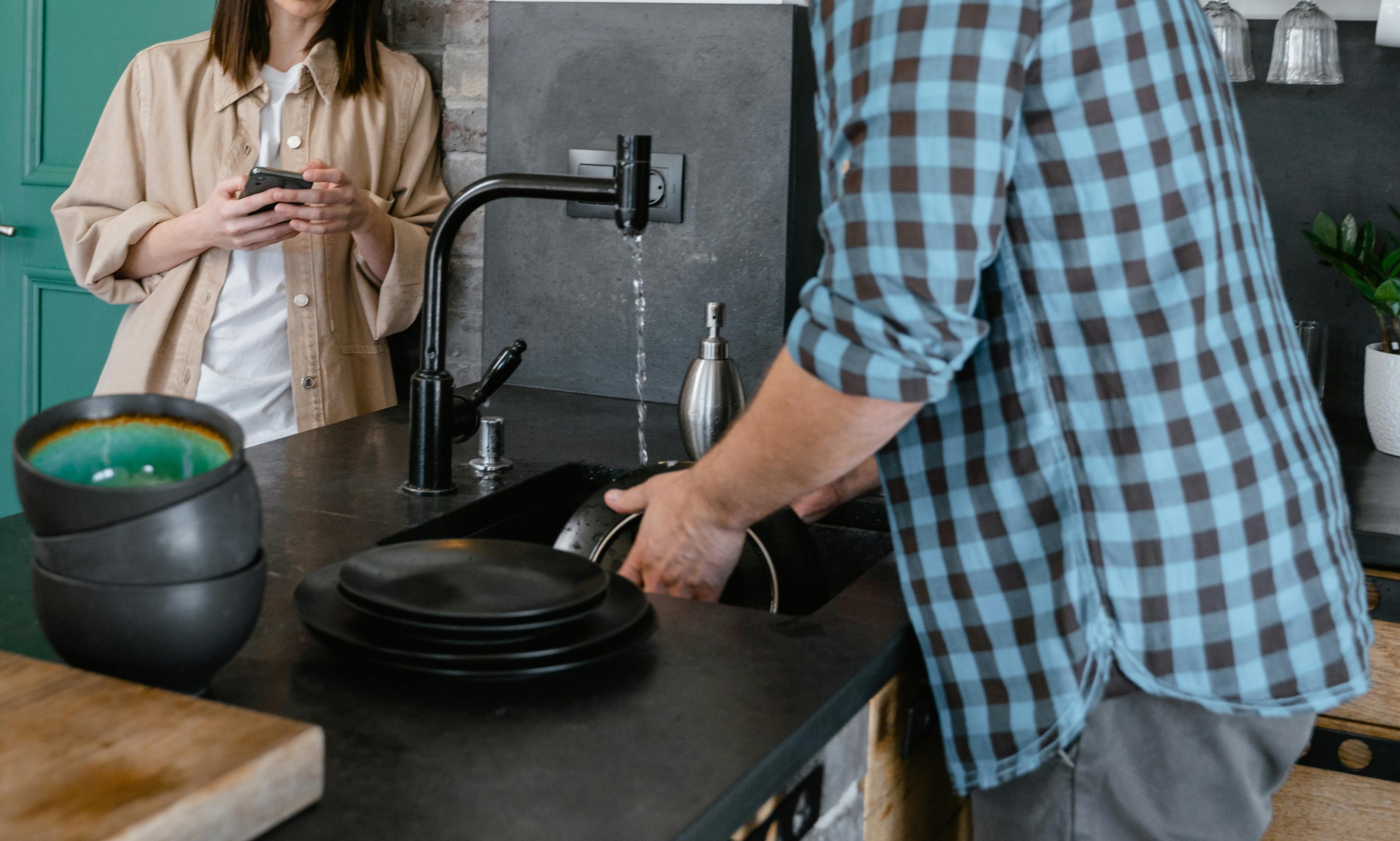 A woman observing a man washing dishes in the kitchen | Source: Pexels