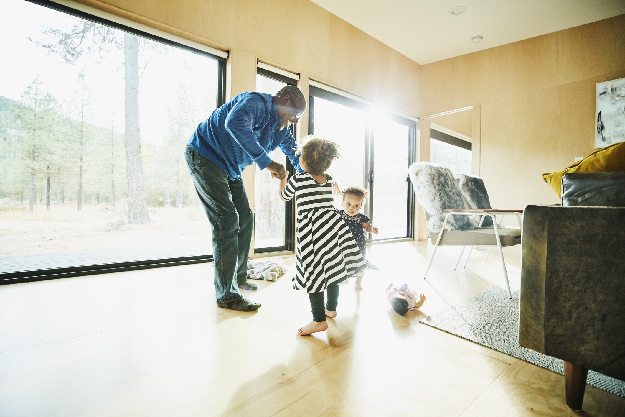 Smiling grandfather dancing with two granddaughters in living room | Photo: Getty Images