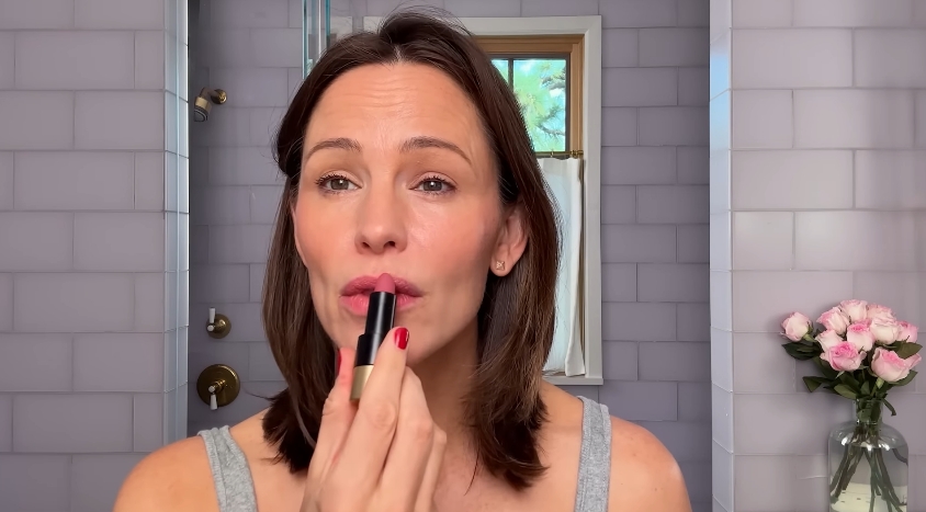 Jennifer Garner applies lipstick while demonstrating some of her favorite beauty products. | Source: YouTube/Vogue