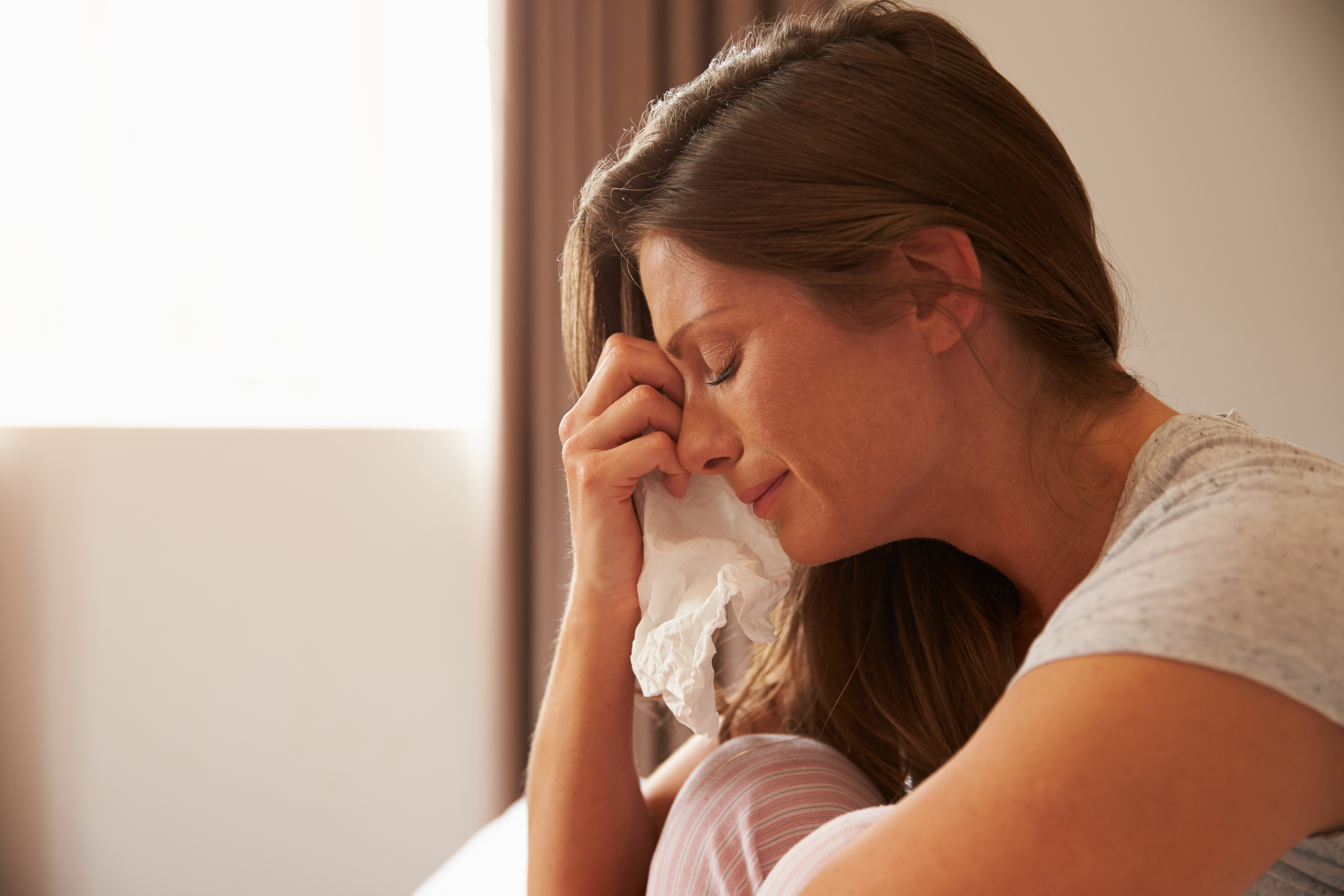 A woman crying as she wipes her tears with a tissue | Source: Shutterstock