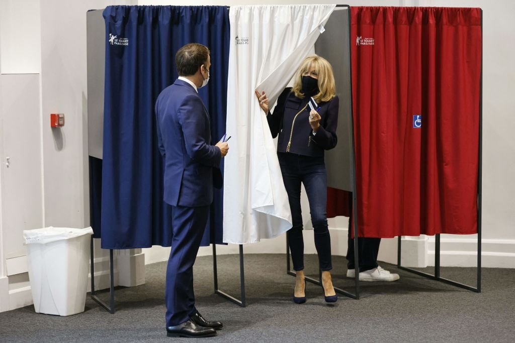 Emmanuel Macron et son épouse Brigitte Macron quittent un isoloir équipé de rideaux anti-covid avant de voter alors qu'ils votent dans un bureau de vote du Touquet le 27 juin 2021. | Photo : Getty Images