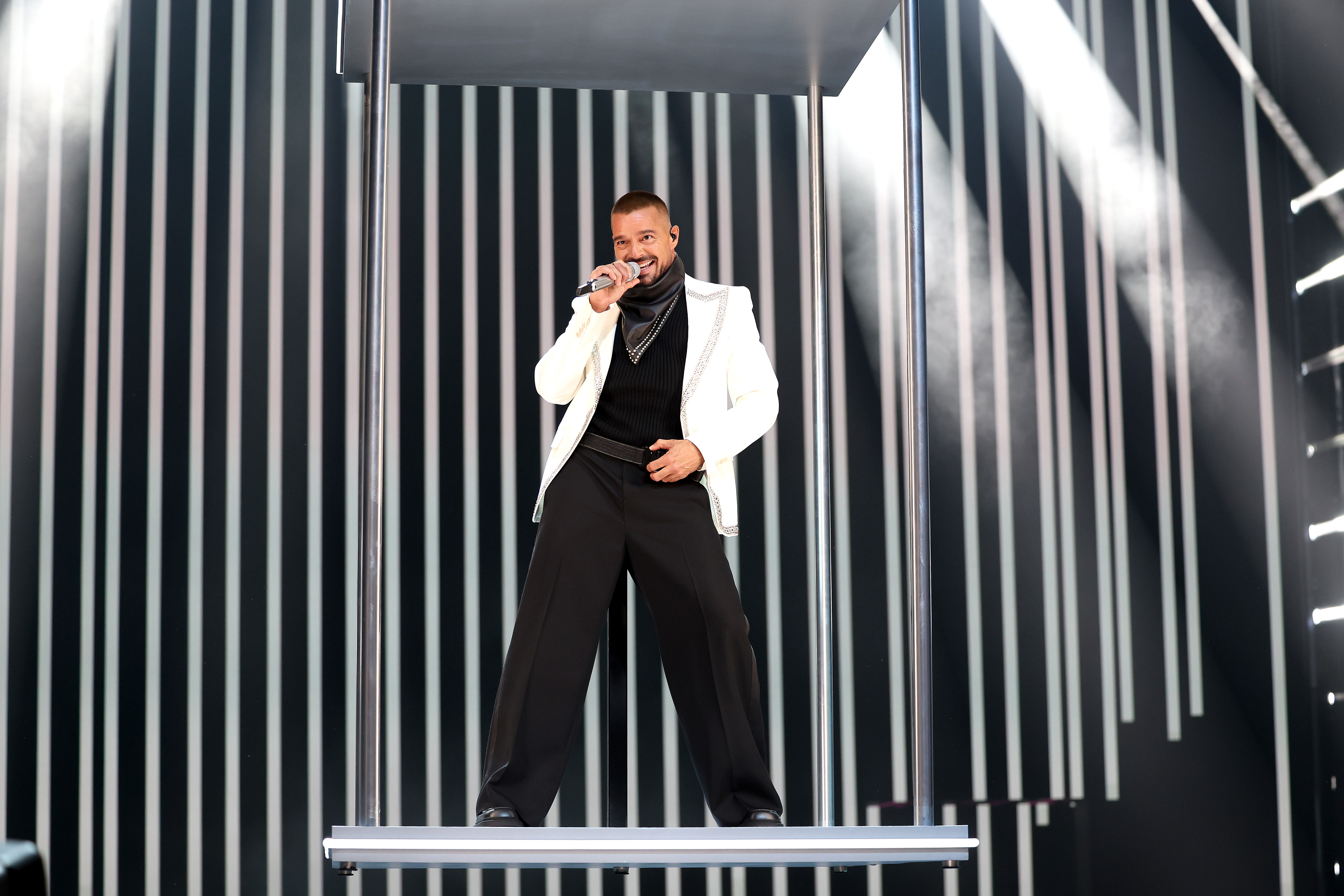 Ricky Martin performs onstage in a white jacket, black turtleneck, and wide-leg pants during the 2025 MTV Video Music Awards at UBS Arena in Elmont, New York.