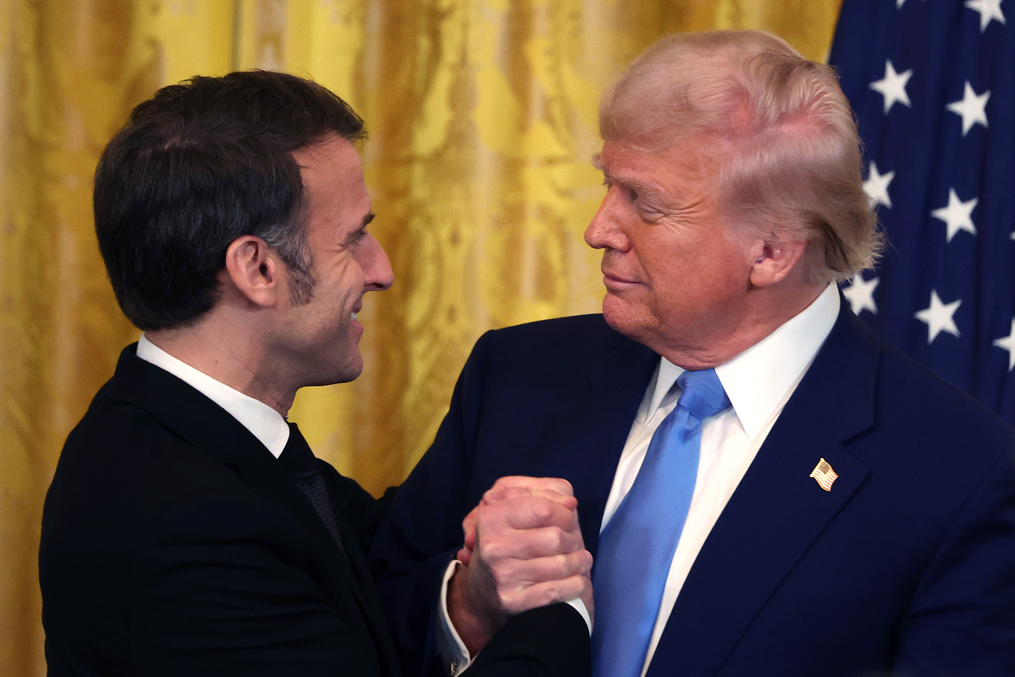 Emmanuel Macron and Donald Trump shaking hands and embracing in the East Room of the White House in Washington, D.C., on February 24, 2025. | Source: Getty Images