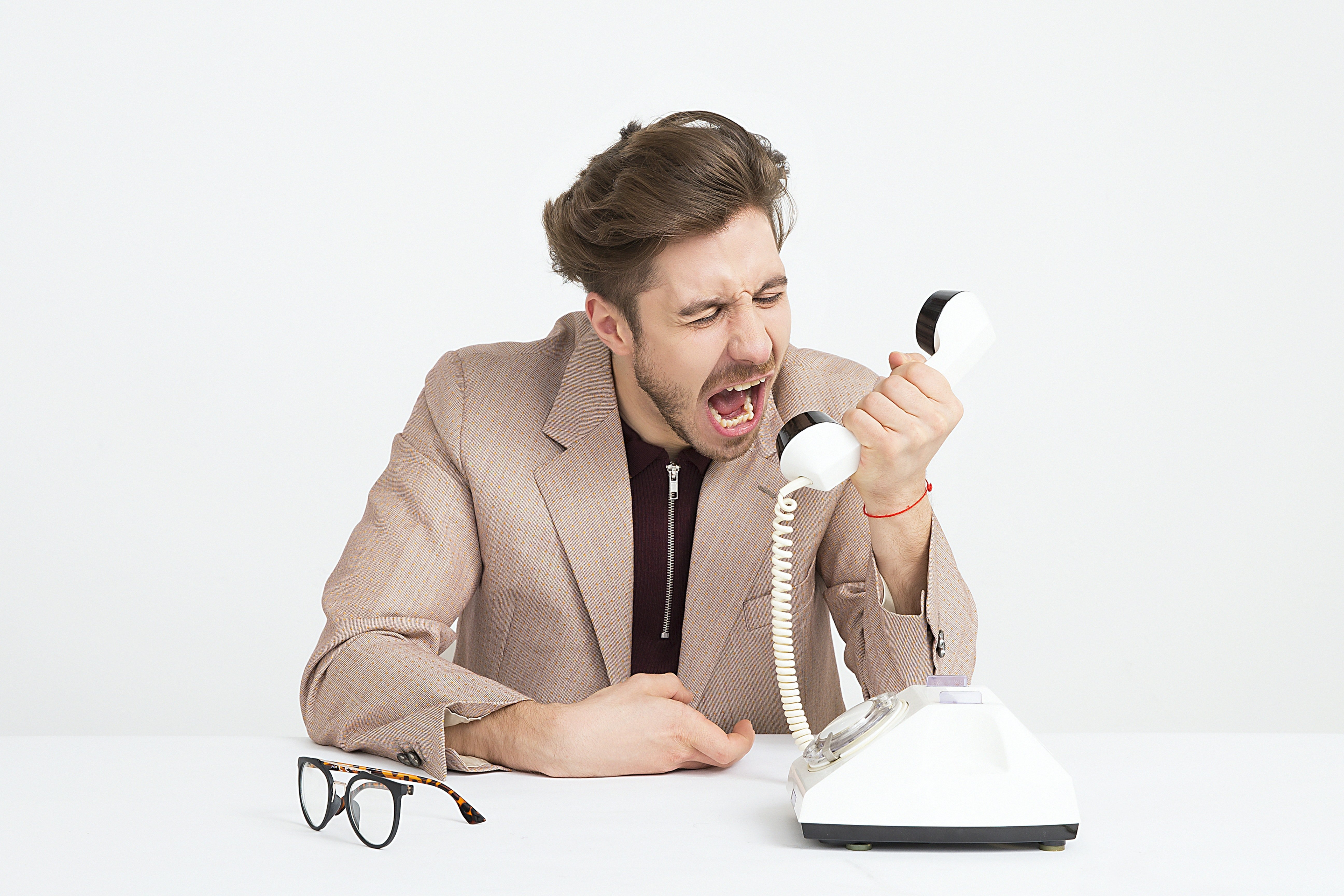 Man Wearing Brown Suit Jacket Mocking on White Telephone| Photo: Pexels
