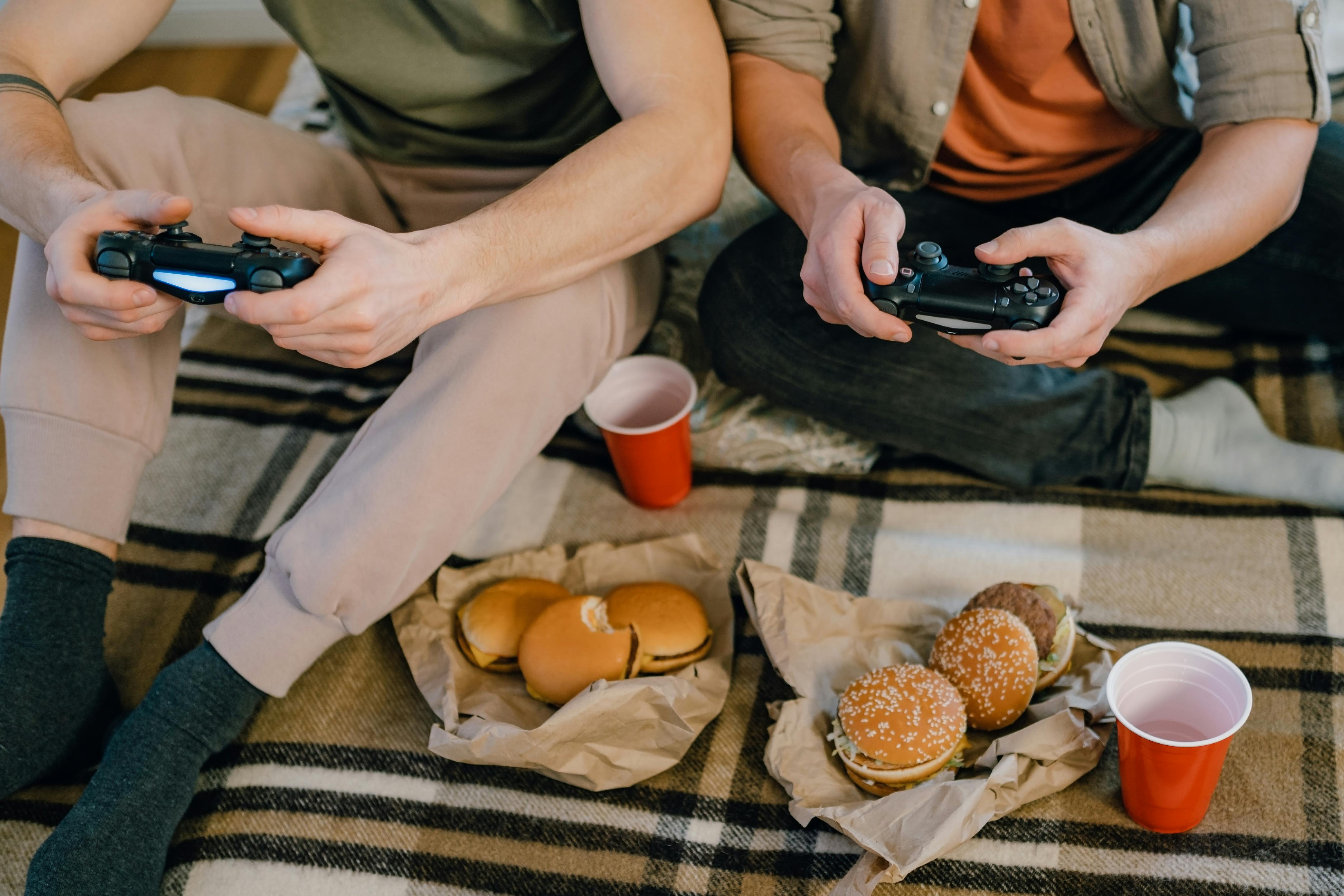 Two men sitting on the floor eating burgers while playing video games | Source: Pexels