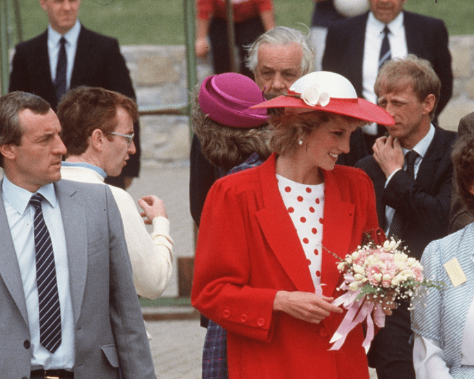 Diana, Princess of Wales, wearing a red jacket with a white and red polka dot dress and a matching hat, with her bodyguard Barry Mannakee (grey suit) at an International Deaf Youth Rally at Atlantic College on June 5, 1985 in Llantwit Major, United Kingdom | Source: Getty Images
