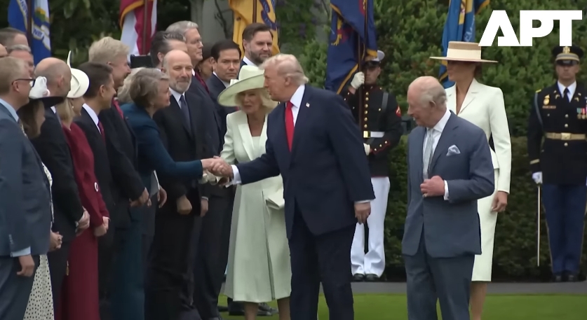 Donald Trump begins greeting officials himself, leaning in for a handshake as Queen Camilla stands just behind his shoulder, waiting for her turn to resume, while King Charles III pauses a few steps ahead. | Source: YouTube/APT
