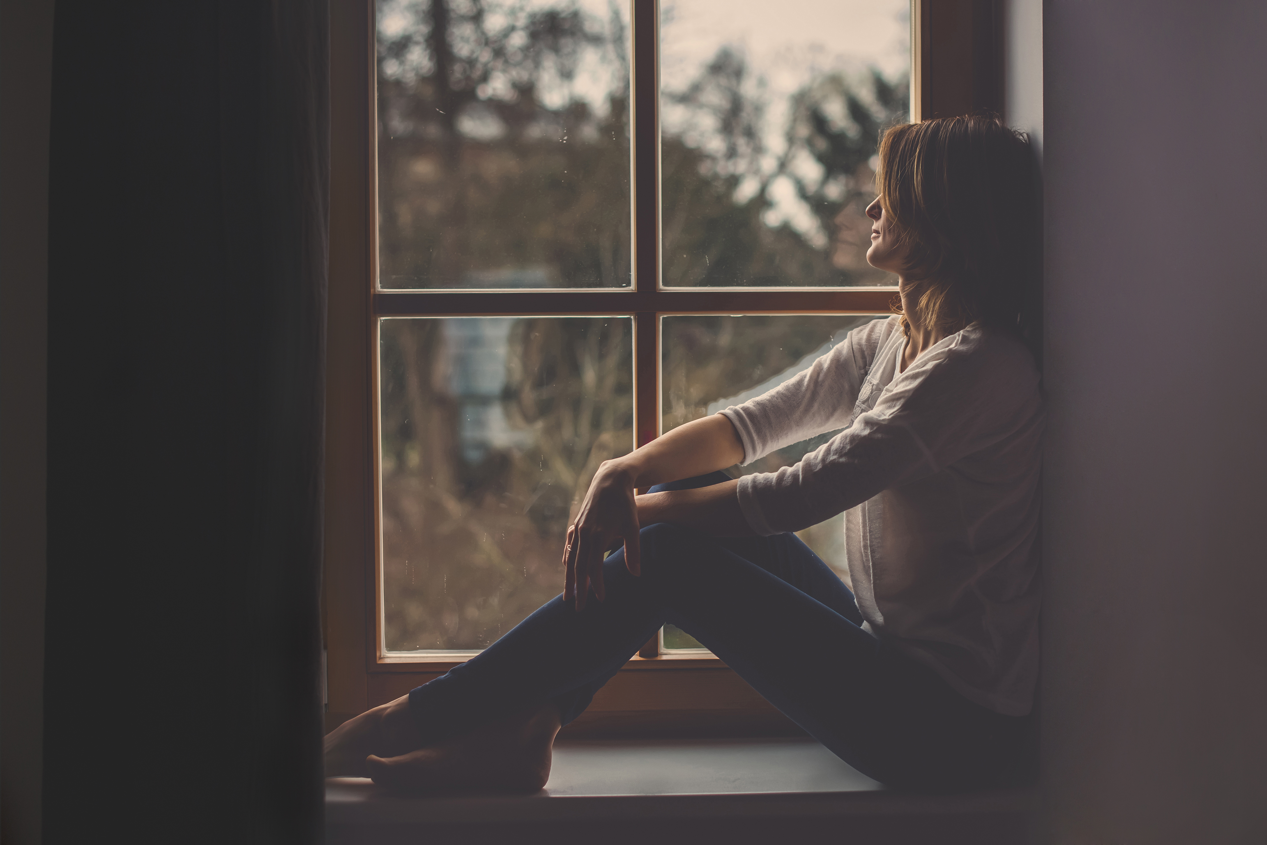 A woman sitting near a window sill looking outside | Source: Shutterstock