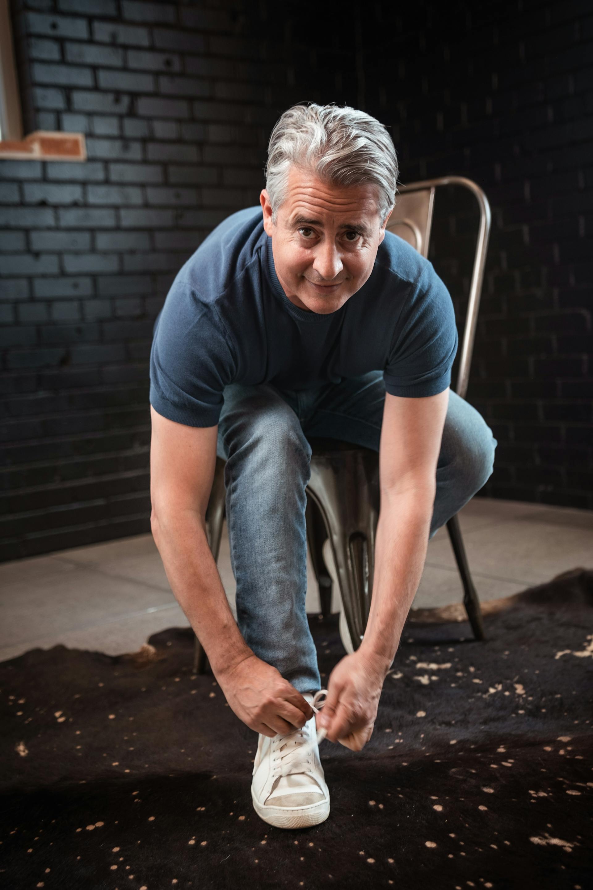 A middle-aged man sitting on a chair and tying his shoe | Source: Pexels