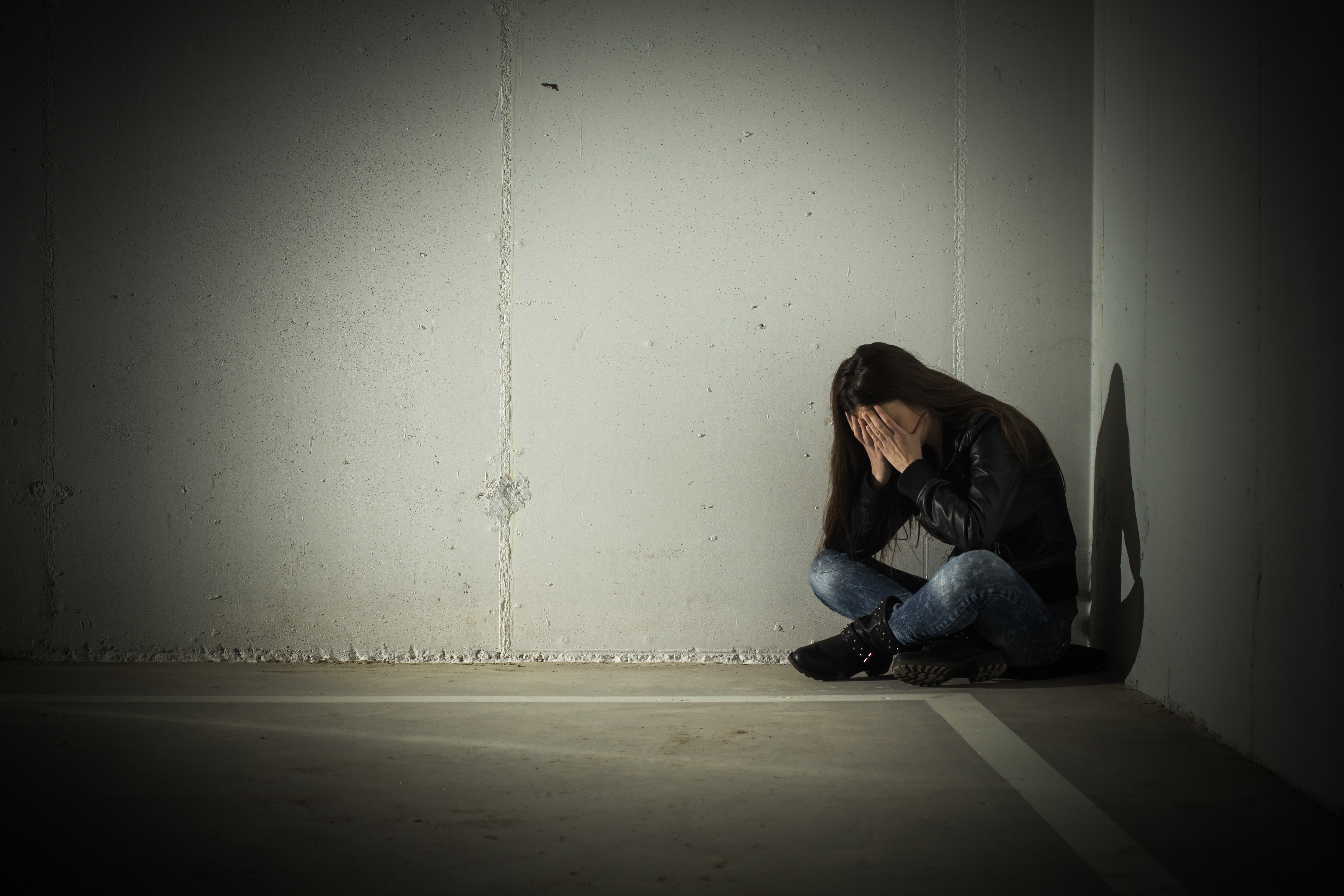 Depressed teenage girl with hands over face sitting in the corner | Source: Shutterstock.com