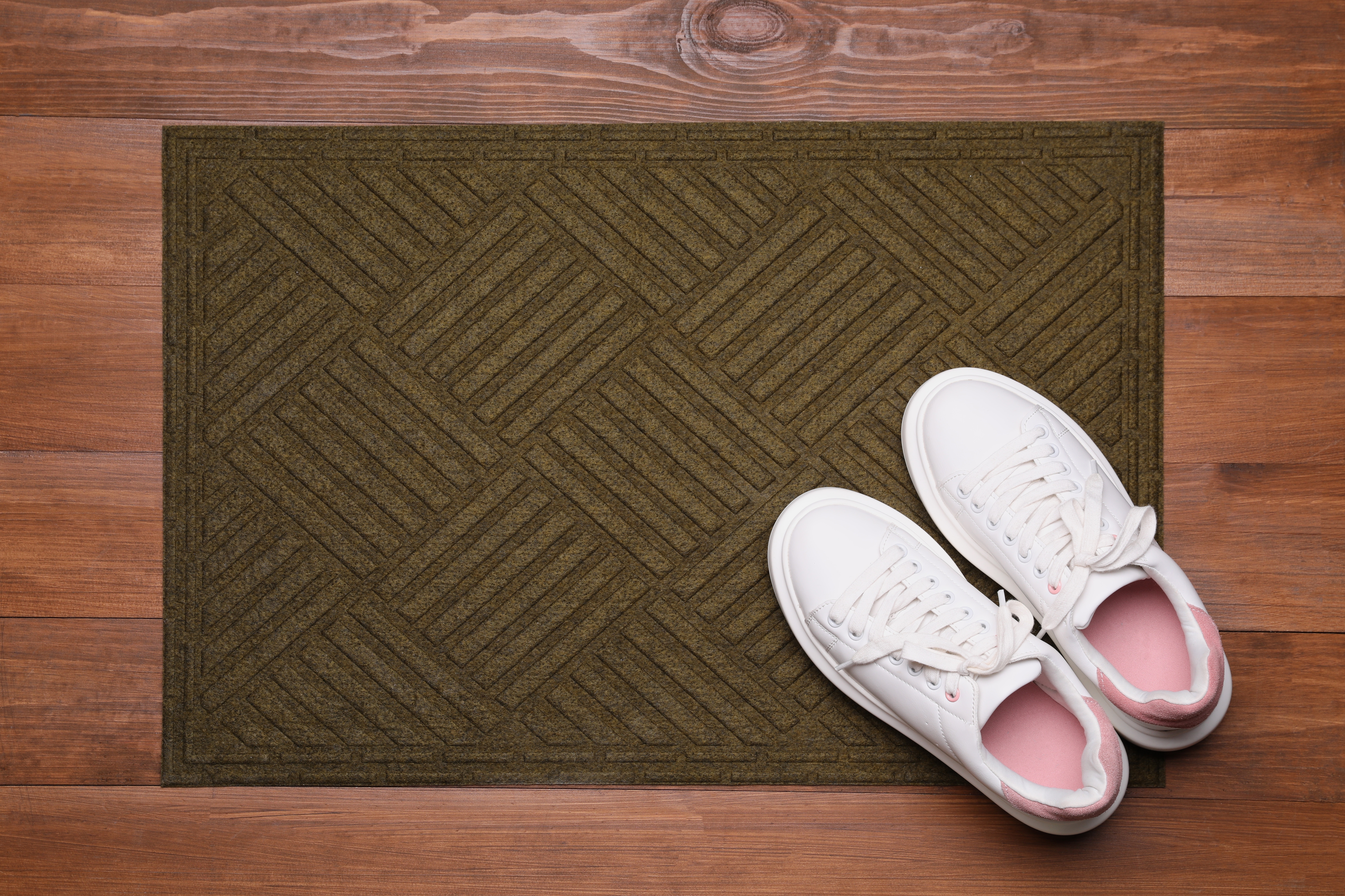 A pair of white sneakers are placed on a door mat lying on the wooden floor | Source: Shutterstock