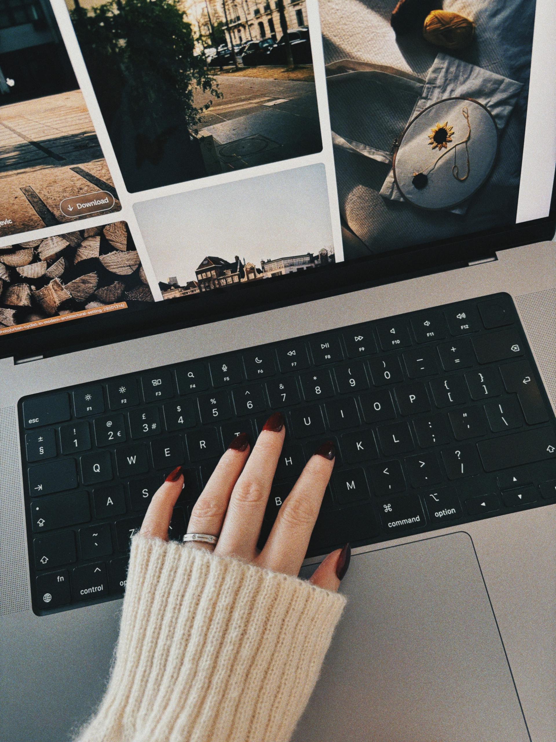 A person with red-manicured nails and a white sweater using their laptop | Source: Pexels