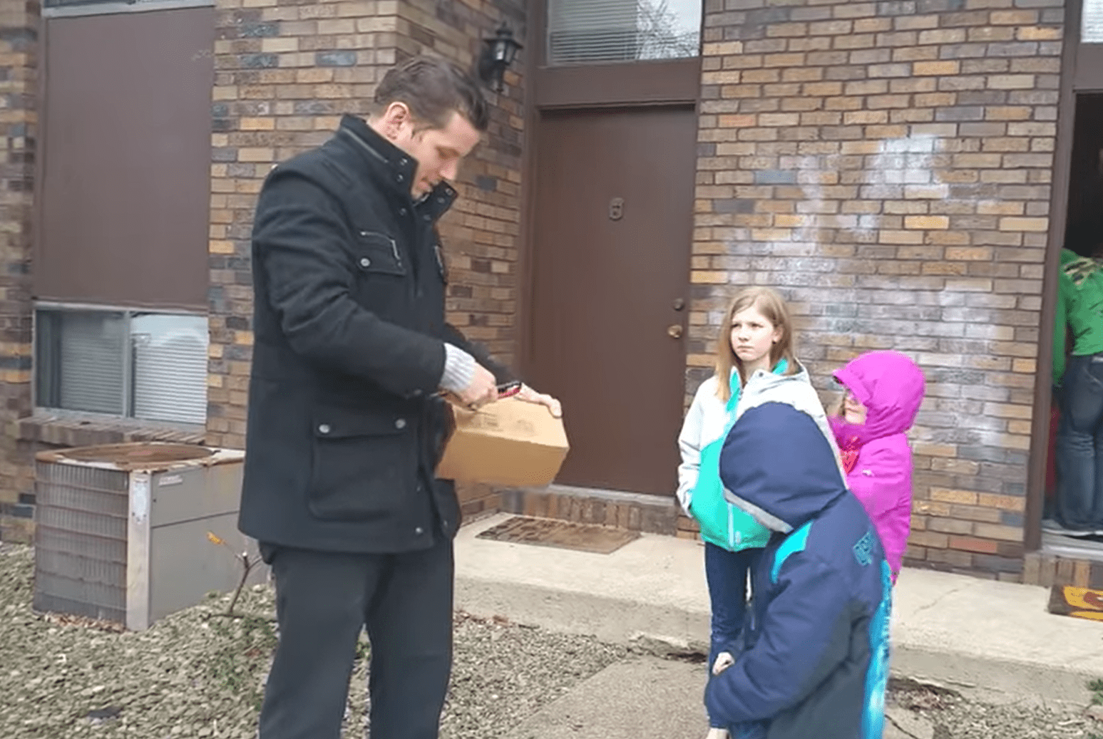 Opie Hughes opening the box with the EnChroma glasses as his children stand in front of him. | Source: youtube.com/Kat