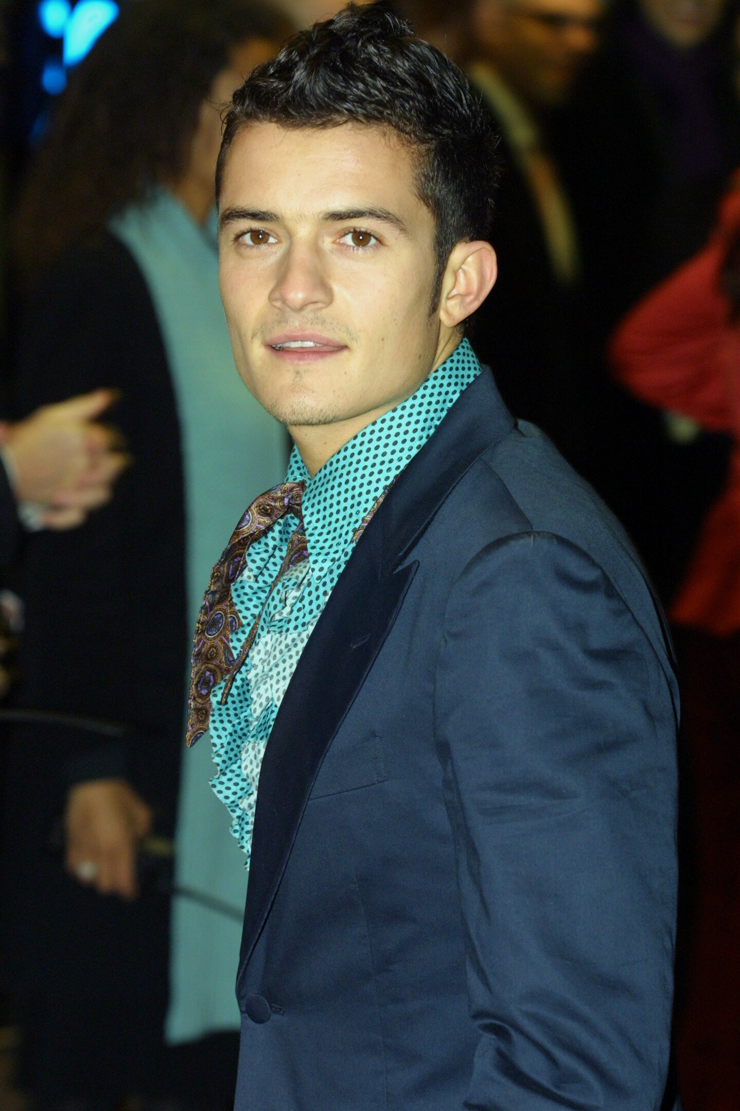Orlando Bloom attends the London premiere of The Lord of the Rings: The Fellowship of the Ring in 2001, wearing a navy suit layered over a patterned turquoise shirt and scarf, his relaxed expression giving him a confident, fashion-forward look.