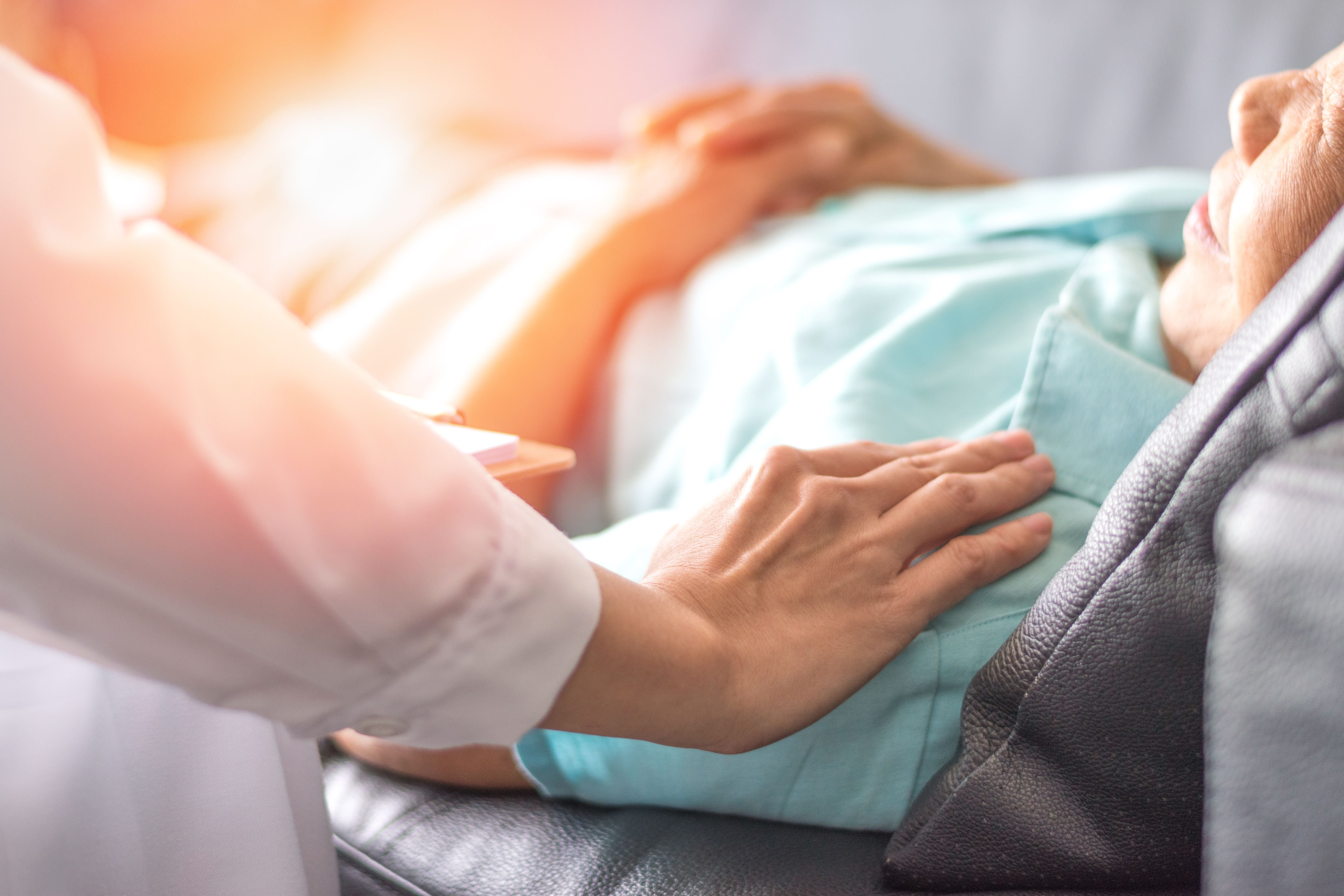 A doctor' hand on a bedridden patient's shoulder.| Source: Shutterstock