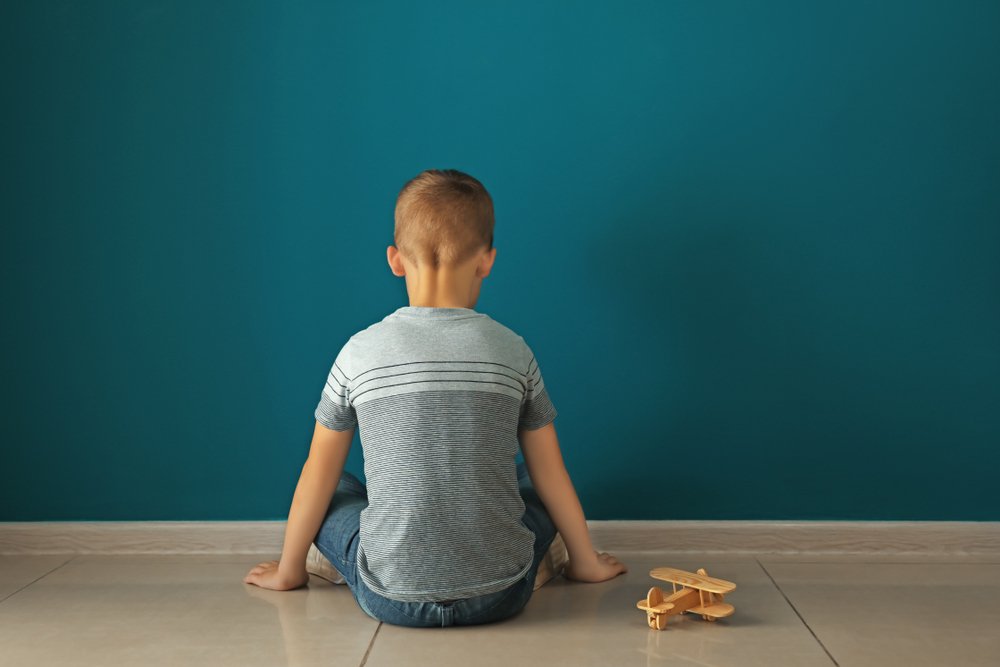 Autism Concept: Little boy sitting near dark wall in empty room | Source: Shutterstock