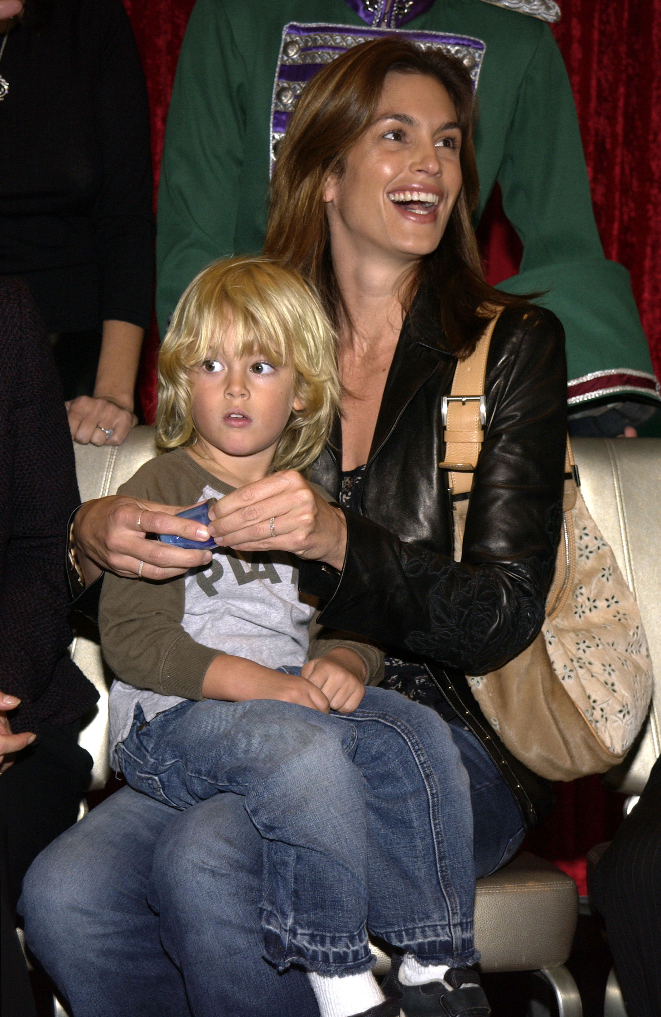 Cindy Crawford and a young Presley Gerber attended American Ballet Theatre's "The Nutcracker" Family Day Benefit in 2002, sharing a light-hearted moment from the front row. With his tousled blonde hair, wide eyes, and casual outfit, Presley sat comfortably on his mother's lap as she laughed beside him — a picture of childhood innocence and maternal pride at a festive New York event.