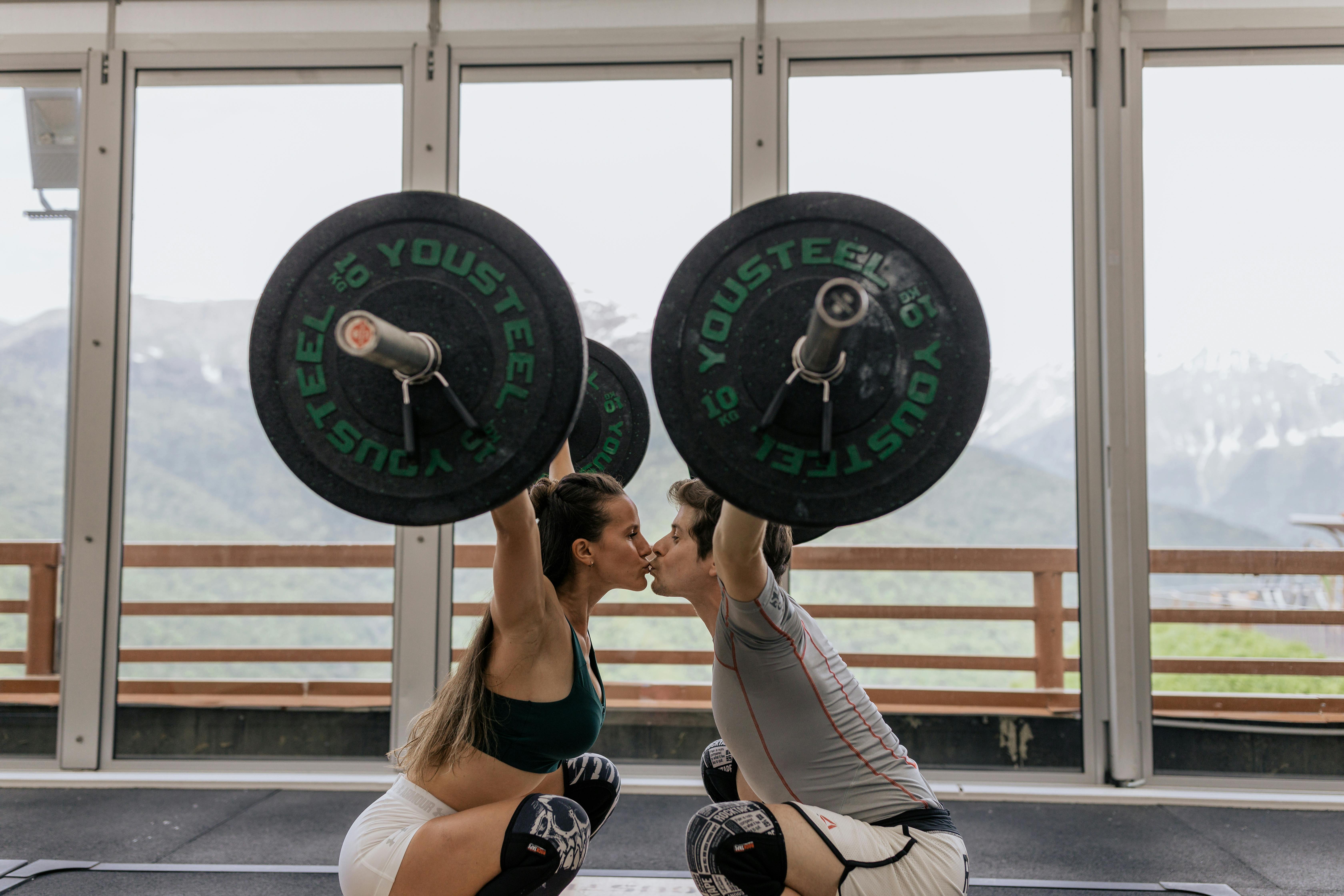 A couple kissing while lifting barbells | Source: Pexels