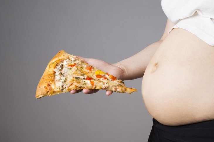 Mujer embarazada con slice de pizza. | Imagen: Shutterstock