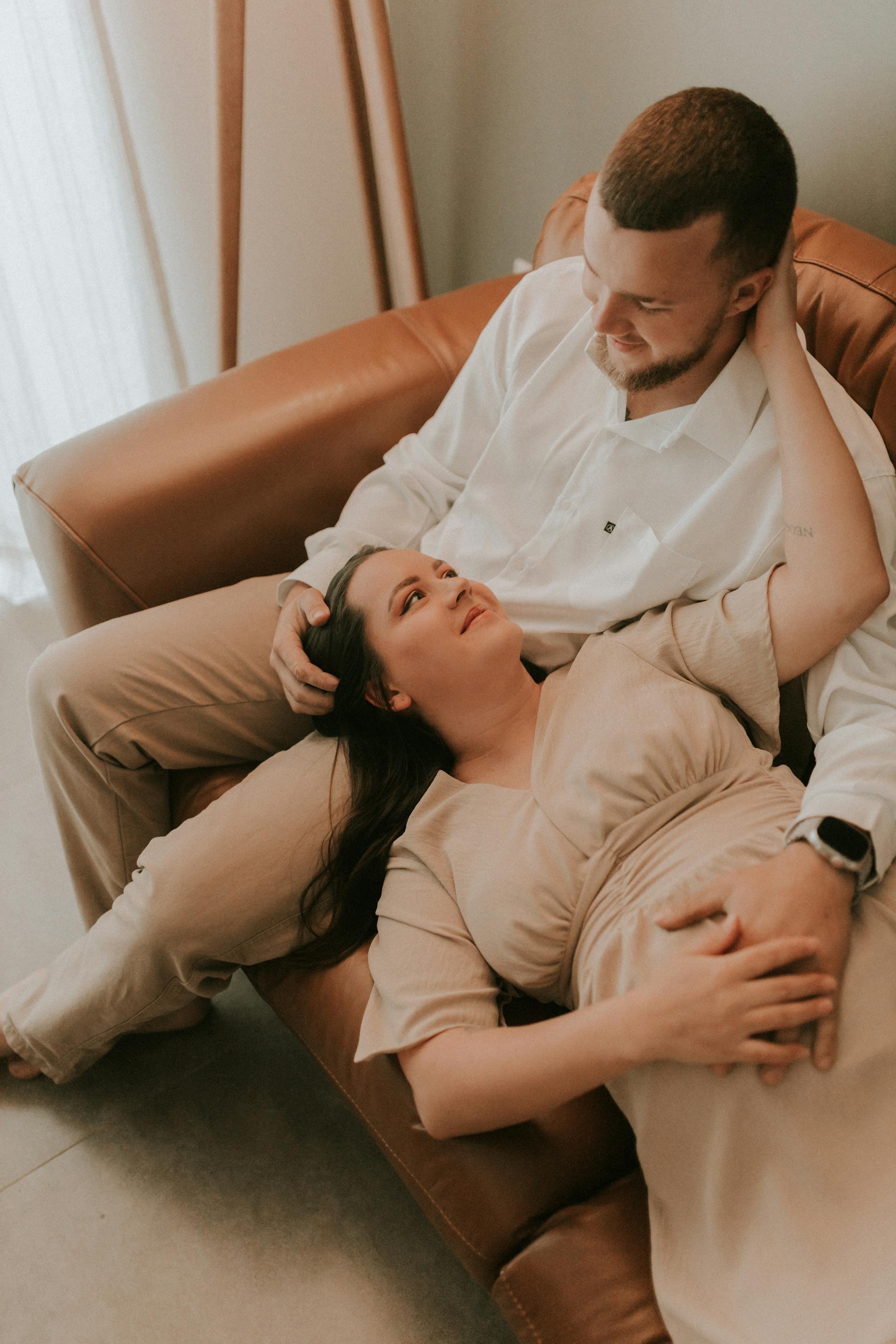 A pregnant woman lying on her husband's lap on a sofa | Source: Pexels