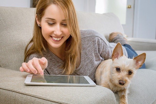 Woman uses tablet while dog lies next to her | Photo: Pixabay