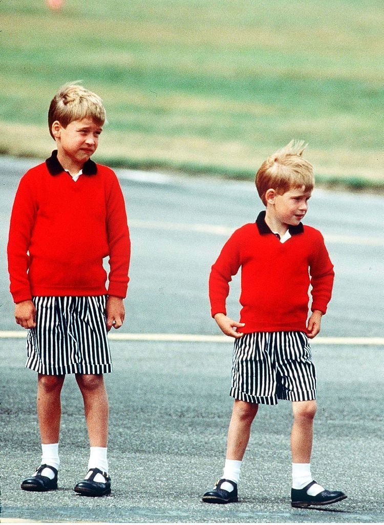 Prince William and Prince Harry, wearing identical red jumpers and stripey shorts, arrive at Aberdeen Airport. | Source: Getty Images