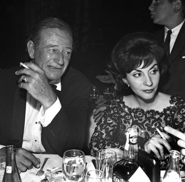 John Wayne y Pilar Palette el 22 de julio de 1961 en el club nocturno Cocoanut Grove en Los Ángeles, California. | Foto: Getty Images