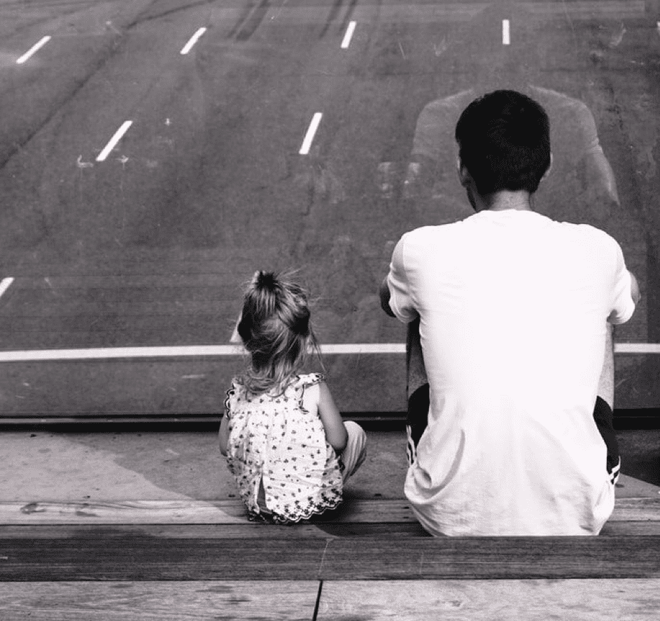 Ein kleines Mädchen sitzt zusammen mit ihrem Vater. | Quelle: Pexels