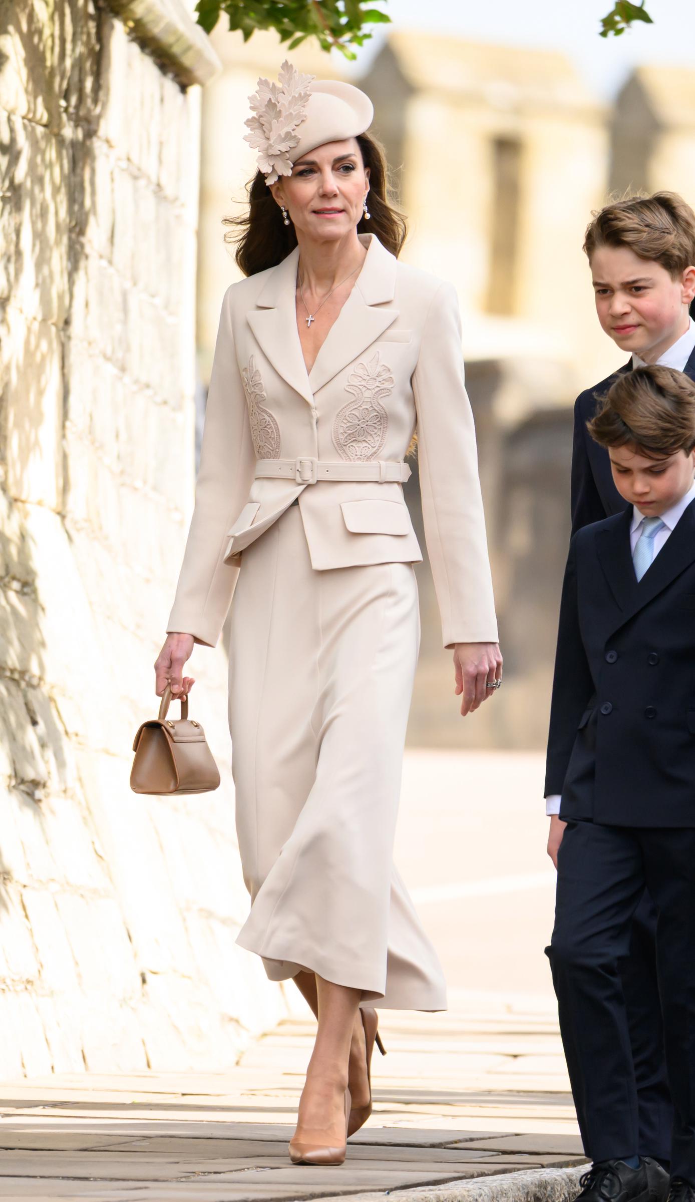 A purposeful stride along the Windsor Castle grounds, and arguably the clearest view of the Princess of Wales's full monochromatic look from collar to heel. The structured lace appliqué blazer and the Ralph Lauren pumps all come together in one unbroken sweep of cream. Prince George trails just behind her to the right, and even at this angle and distance, the height comparison speaks entirely for itself.