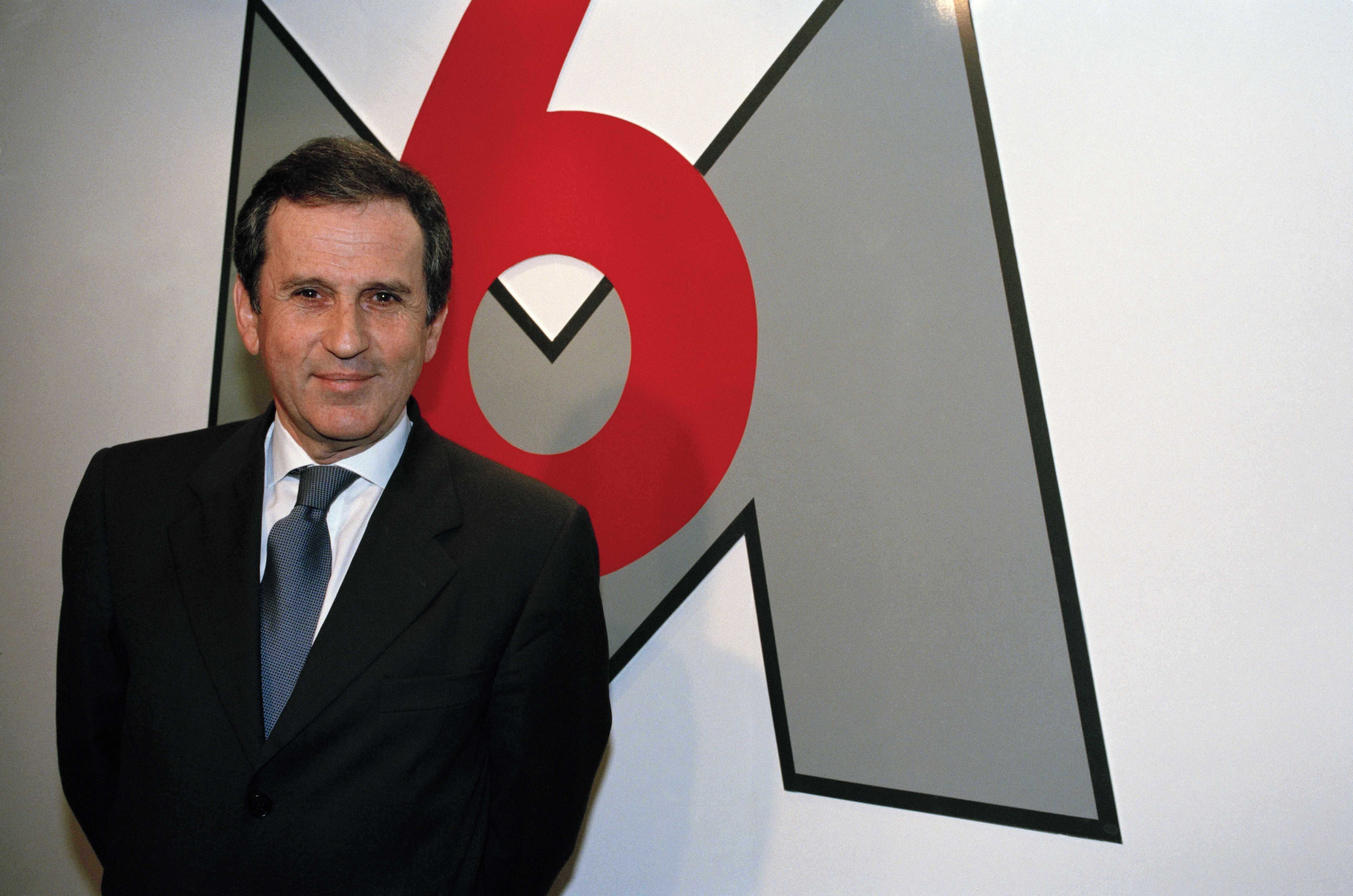 Jean Drucker, journaliste et personnalité de la télévision française, devant le logo de M6 Television, qu'il a fondé. | Photo : Getty Images