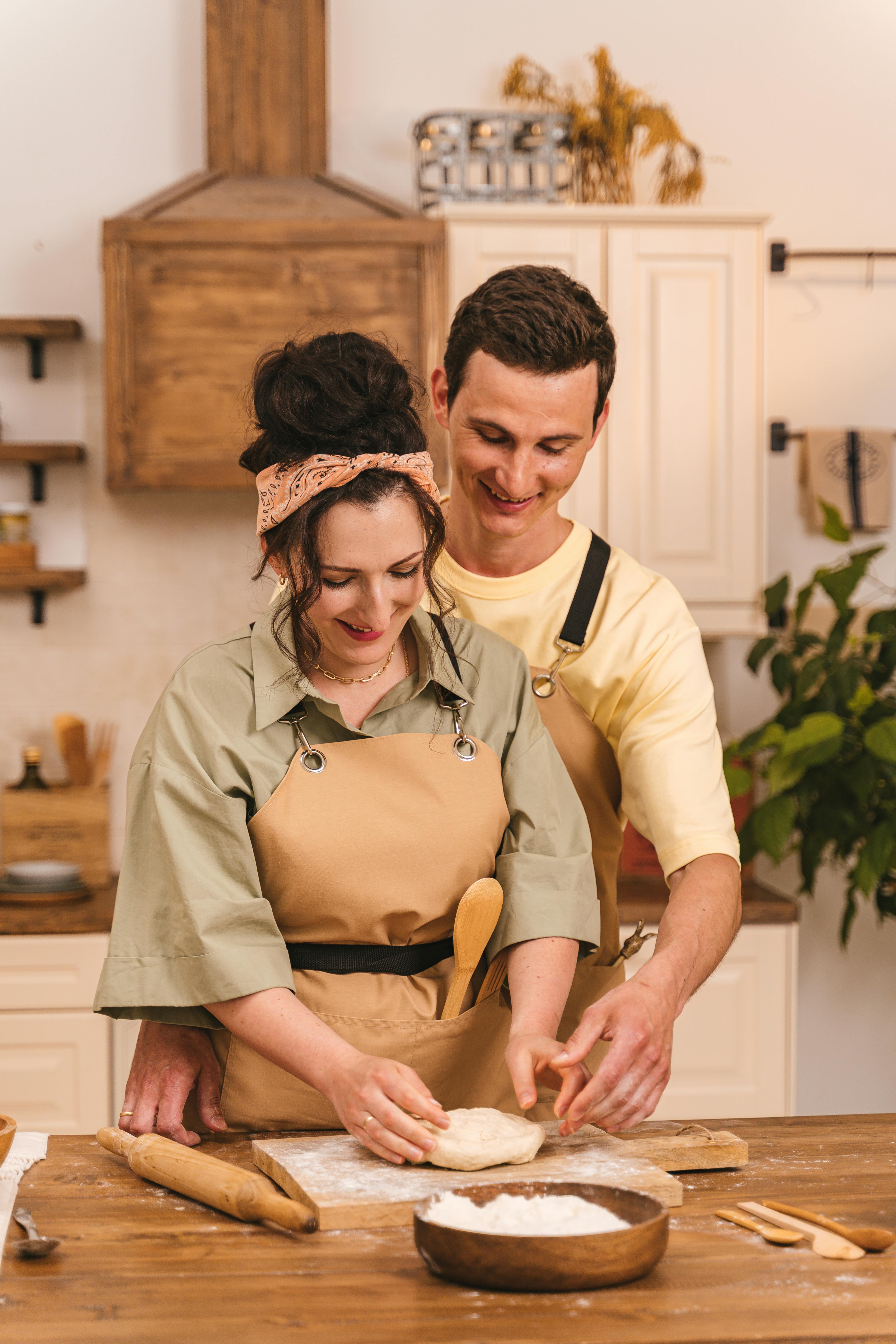 Um homem sorridente olhando para sua esposa cozinhando | Fonte: Pexels