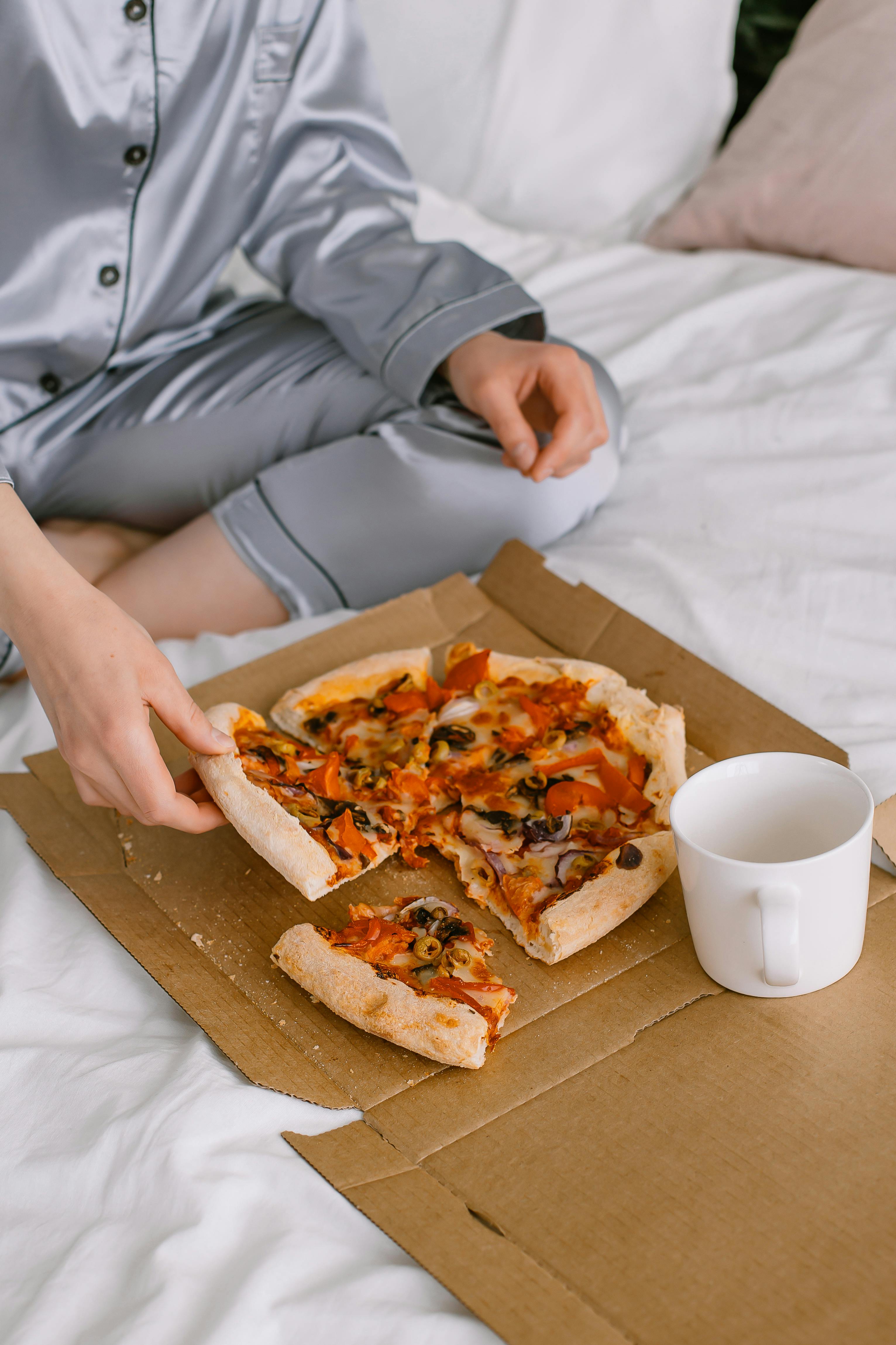 A woman eating pizza in bed | Source: Pexels