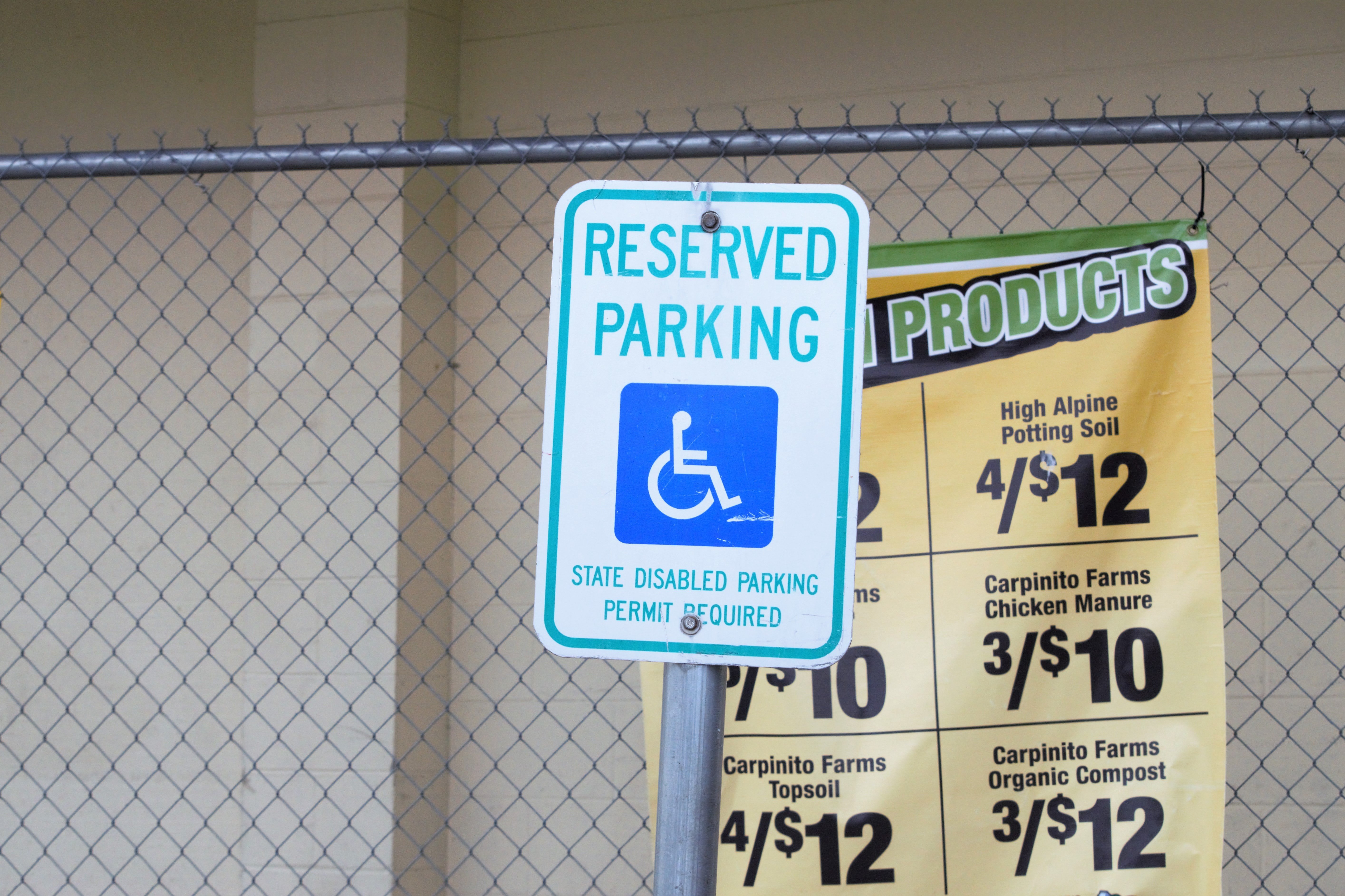 A reserved handicapped parking sign hangs on a fence | Photo: Unsplash/Jennifer Uppendahl