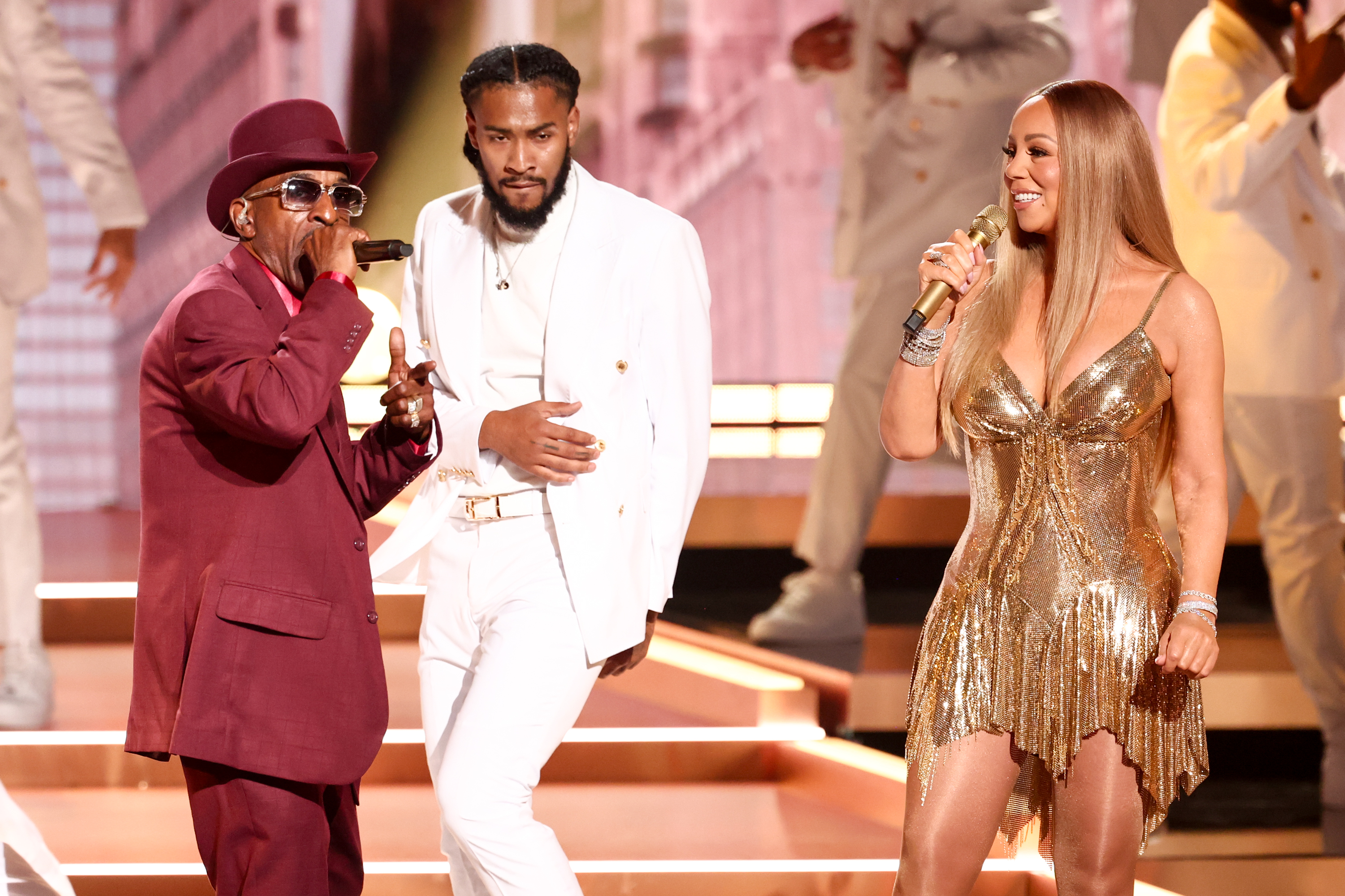 Carey exudes her signature aura as she shares the stage with singer Rakim. The shot captures her, Rakim, and a dancer, yet Carey’s captivating glow naturally draws the spotlight as she transports the audience back to the golden era of pop.